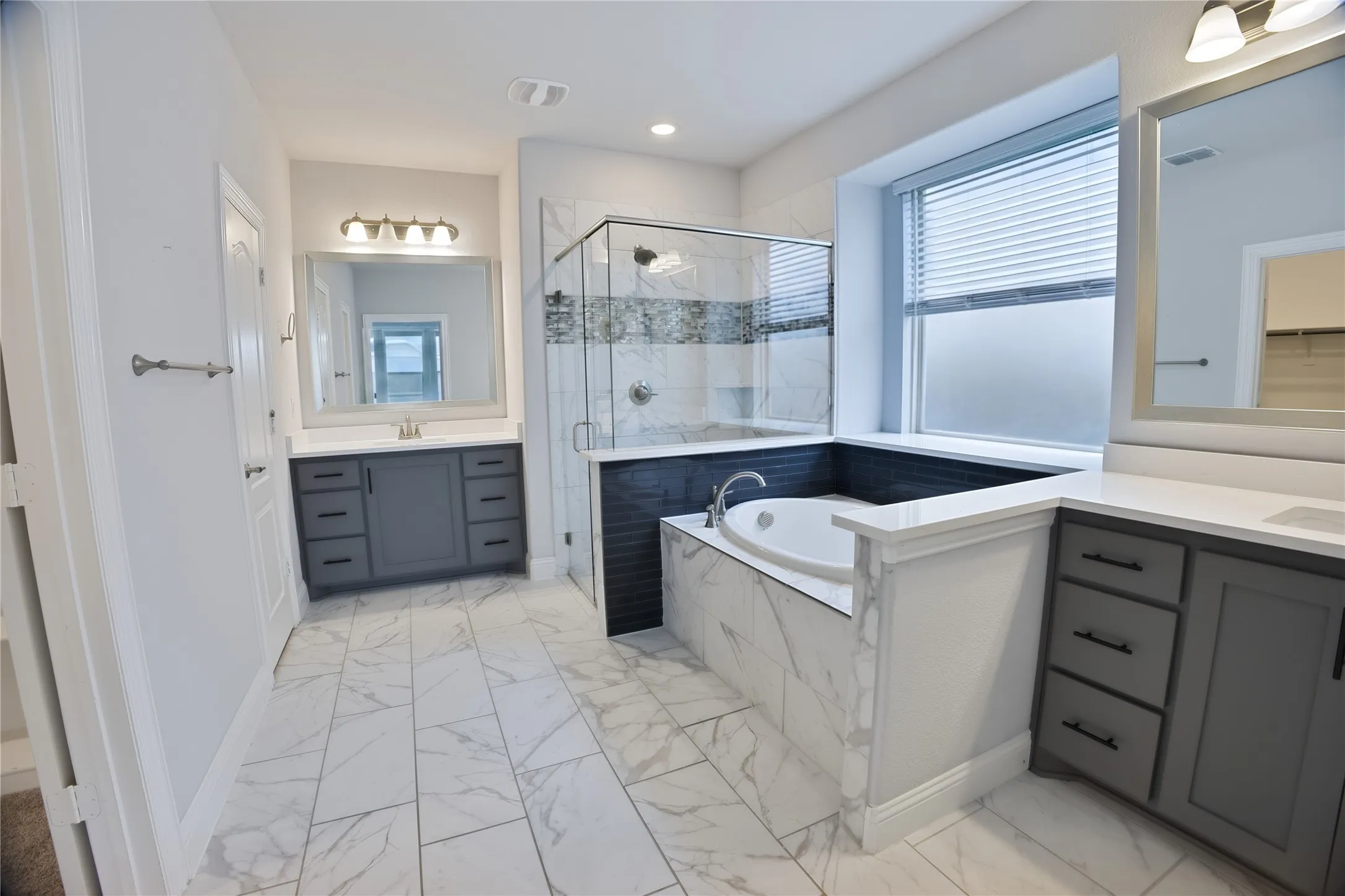 Contemporary bathroom featuring dual vanities with quartz countertops, a built-in soaking tub, a glass-enclosed shower, and large format tile flooring