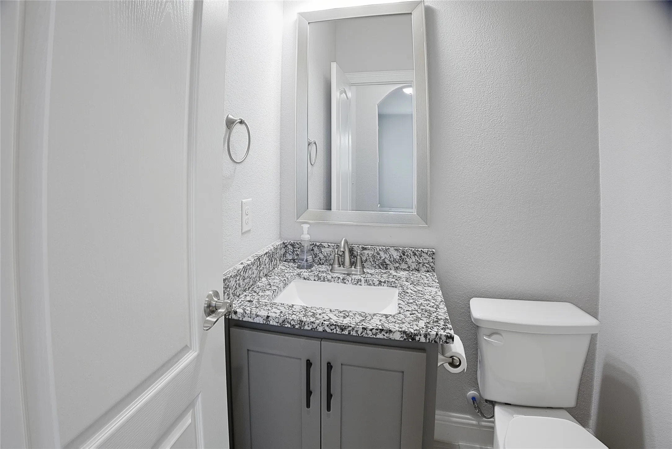 Bathroom featuring a gray vanity with black hardware, a granite-finish countertop, an undermount sink, and a framed mirror