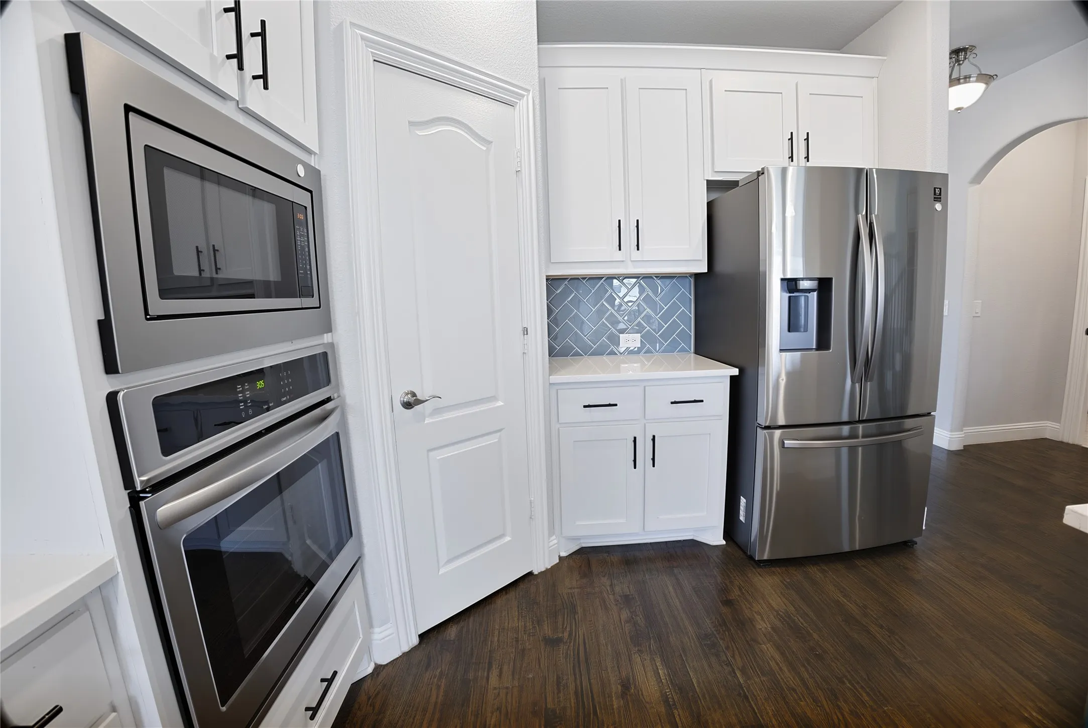Kitchen featuring stainless steel appliances, white cabinetry with dark hardware, a herringbone pattern tile backsplash, and wood-finish flooring