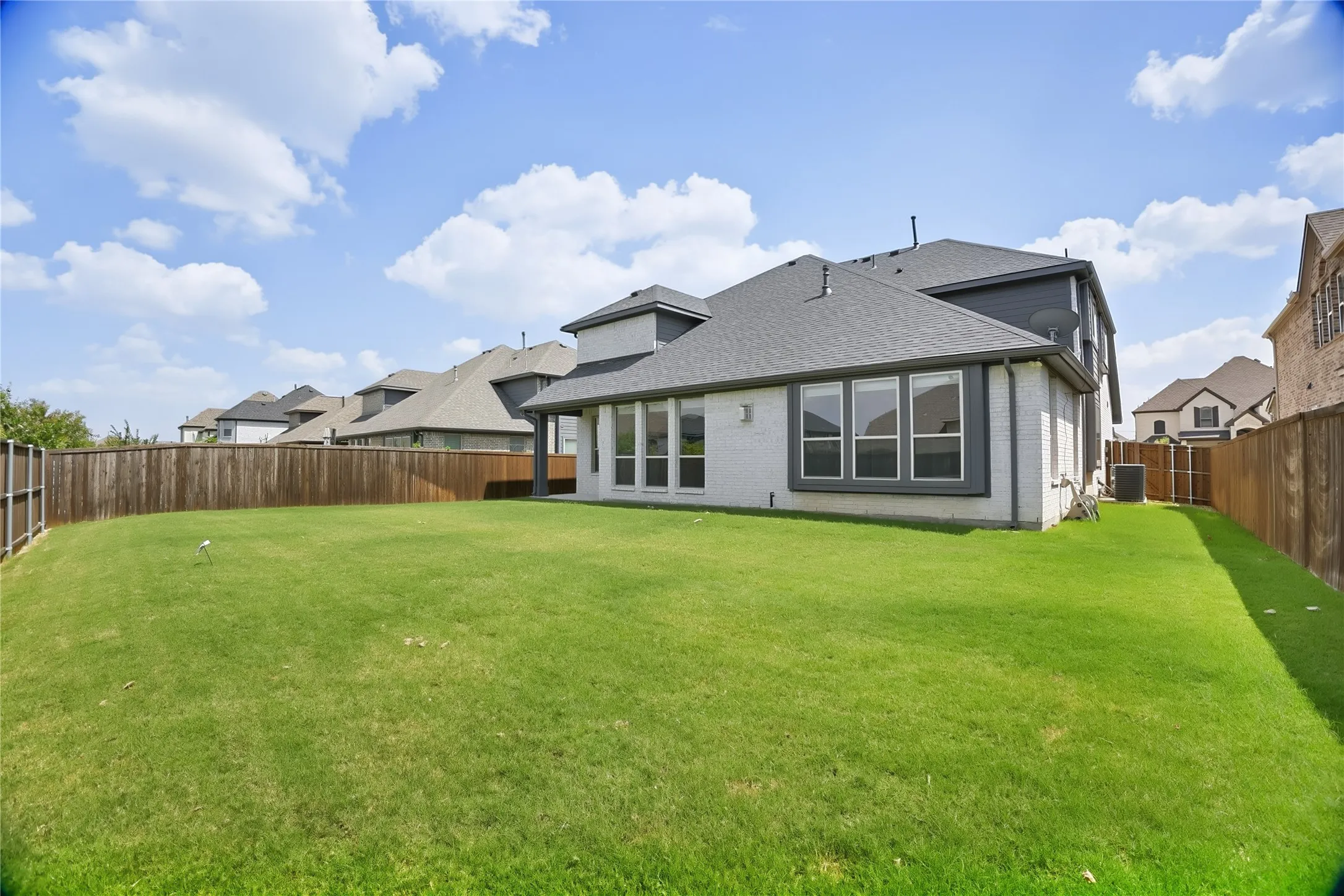 Expansive backyard featuring a lush lawn, privacy fencing, and a white brick exterior with dark trim