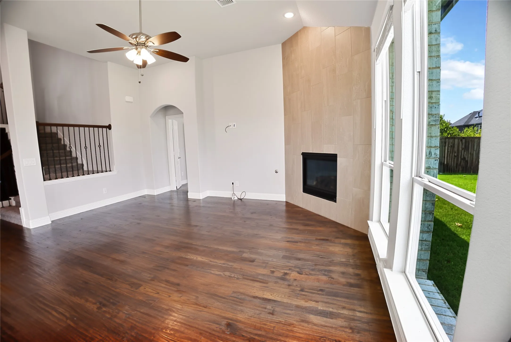 Spacious living area featuring rich wood-finish flooring, a contemporary fireplace with a light-toned tile surround, and multiple large windows