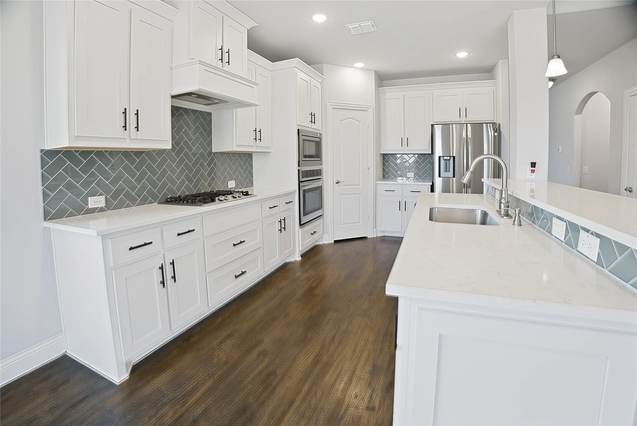 Contemporary kitchen featuring white cabinetry with dark hardware, a herringbone tile backsplash, integrated stainless steel appliances, light-toned countertops, and wood-finish flooring