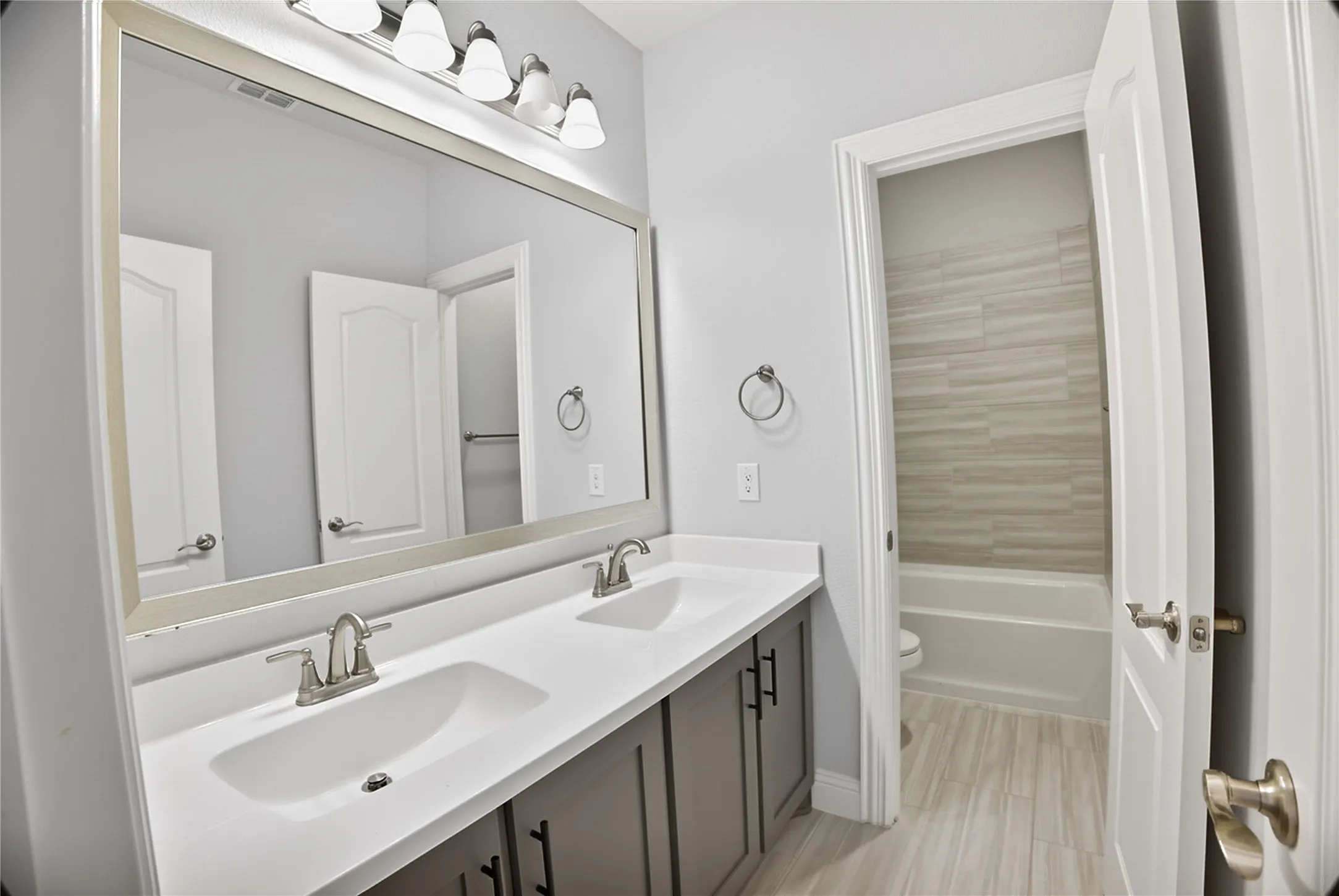 Dual vanity with integrated sinks, brushed nickel fixtures, a large framed mirror, and a five-light vanity bar