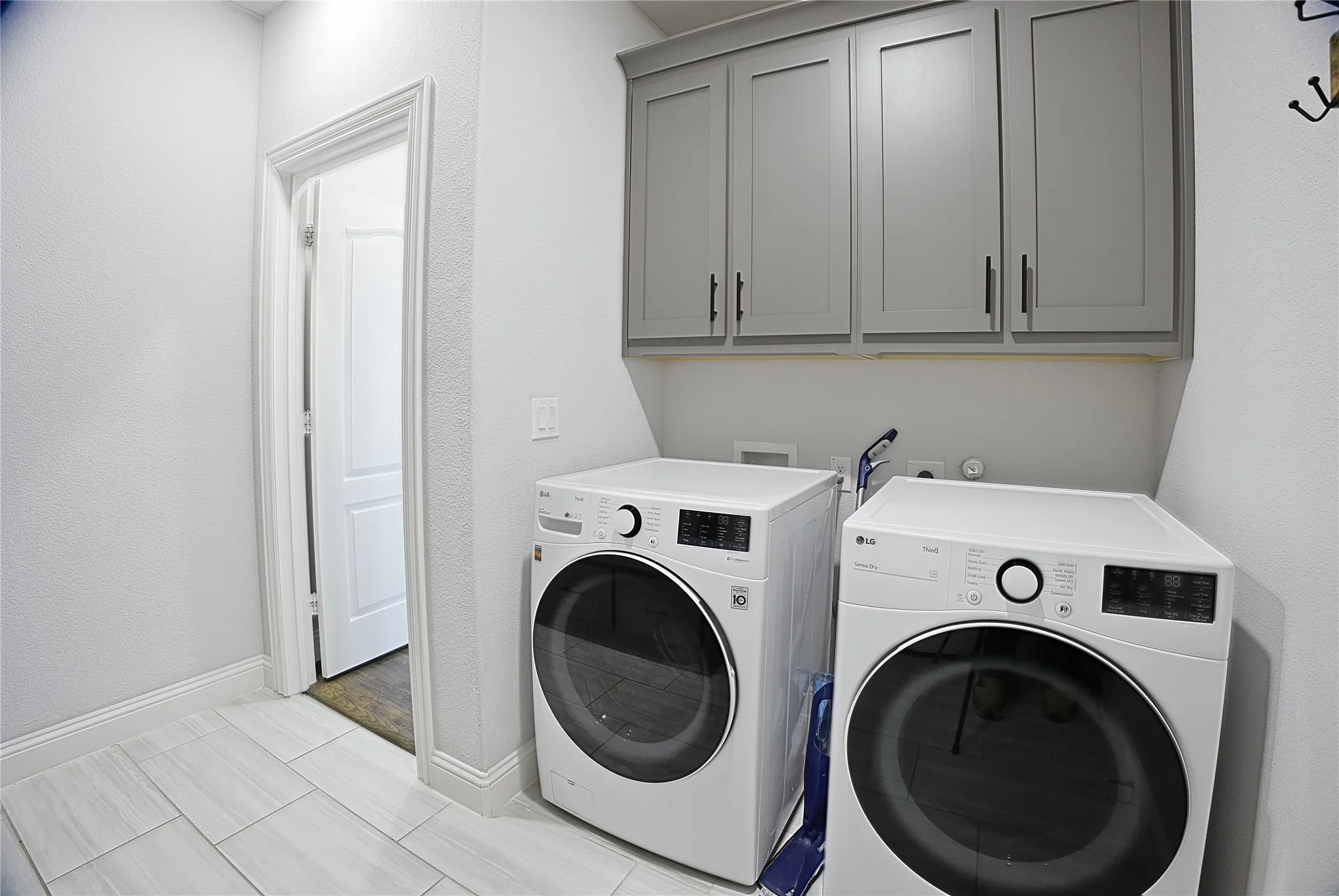 Laundry room featuring light gray wall cabinets with dark hardware, white walls, and light-toned tile flooring