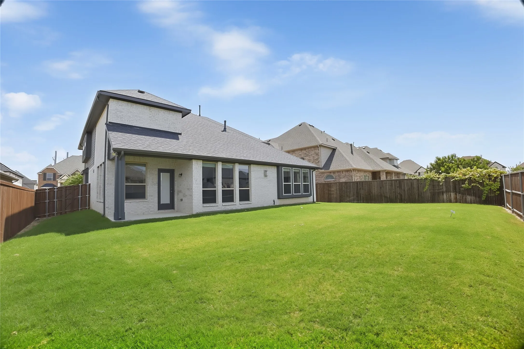 Spacious backyard featuring a manicured lawn, full privacy fencing, and a white brick exterior with dark trim