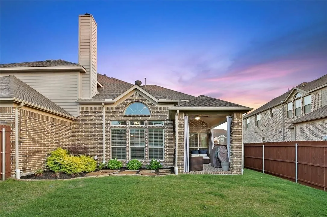 Expansive backyard featuring a covered patio with ceiling fan, brick exterior, large windows with an arched transom, and a private wood fence
