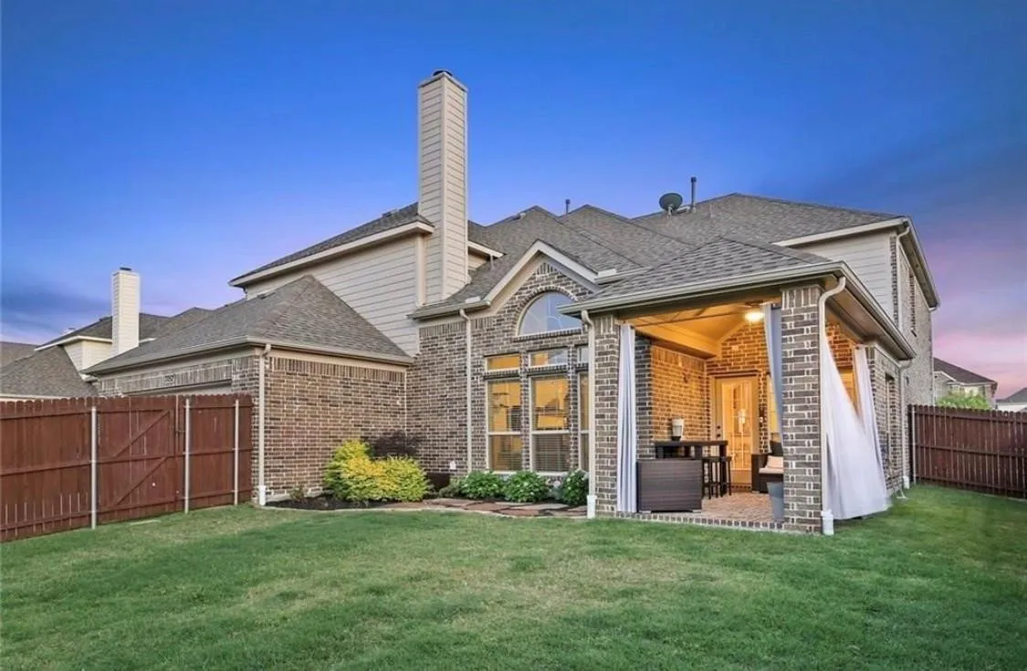 Brick exterior featuring a covered patio, extensive lawn, and a privacy fence