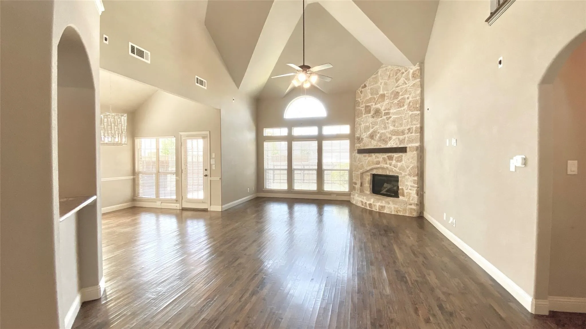 Spacious living area featuring high vaulted ceilings, warm wood-finish flooring, and a stone fireplace with a substantial wood mantel