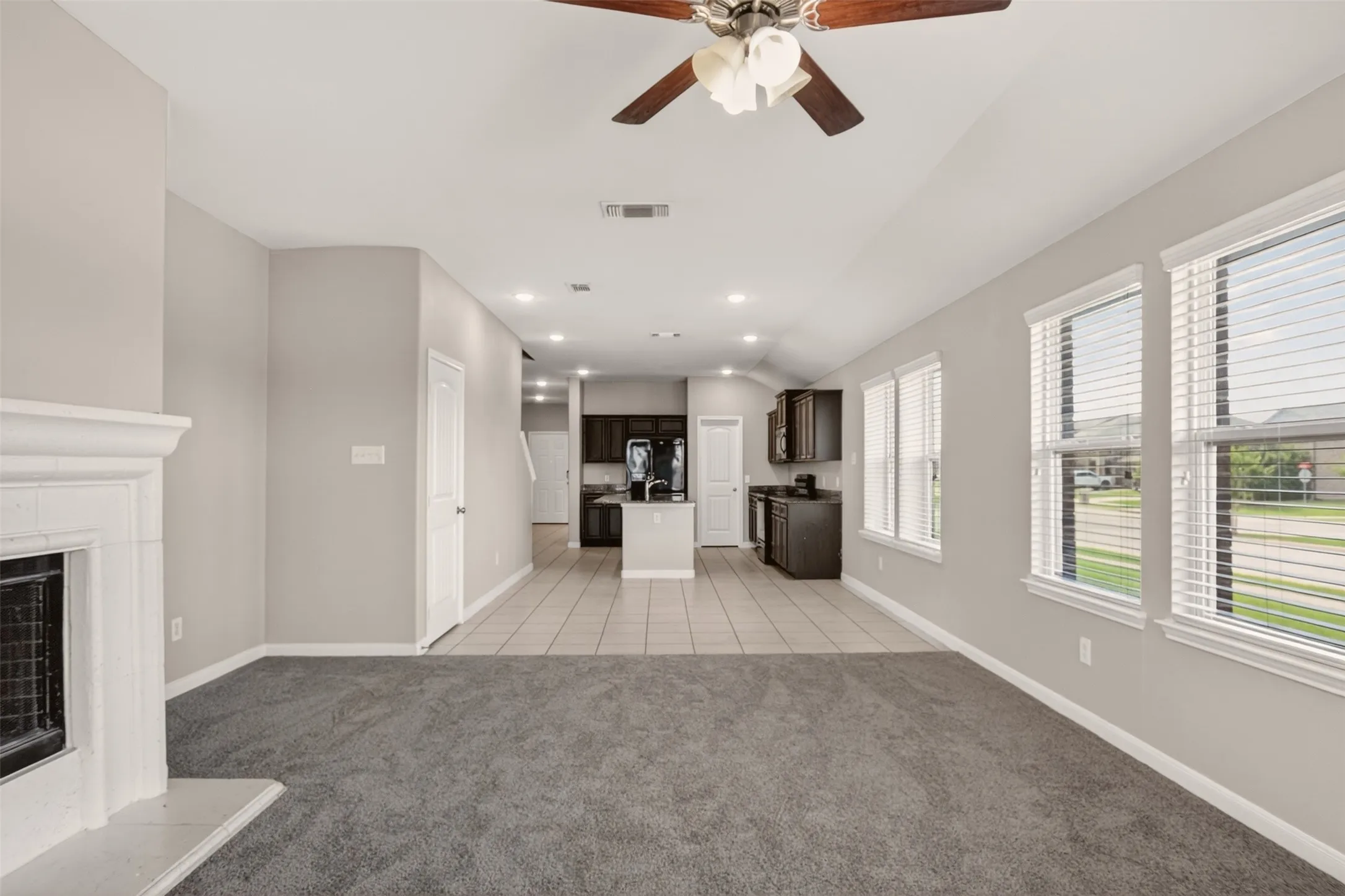 Open-concept living area featuring a white fireplace with mantle, recessed lighting, ceiling fan, and multiple windows with blinds