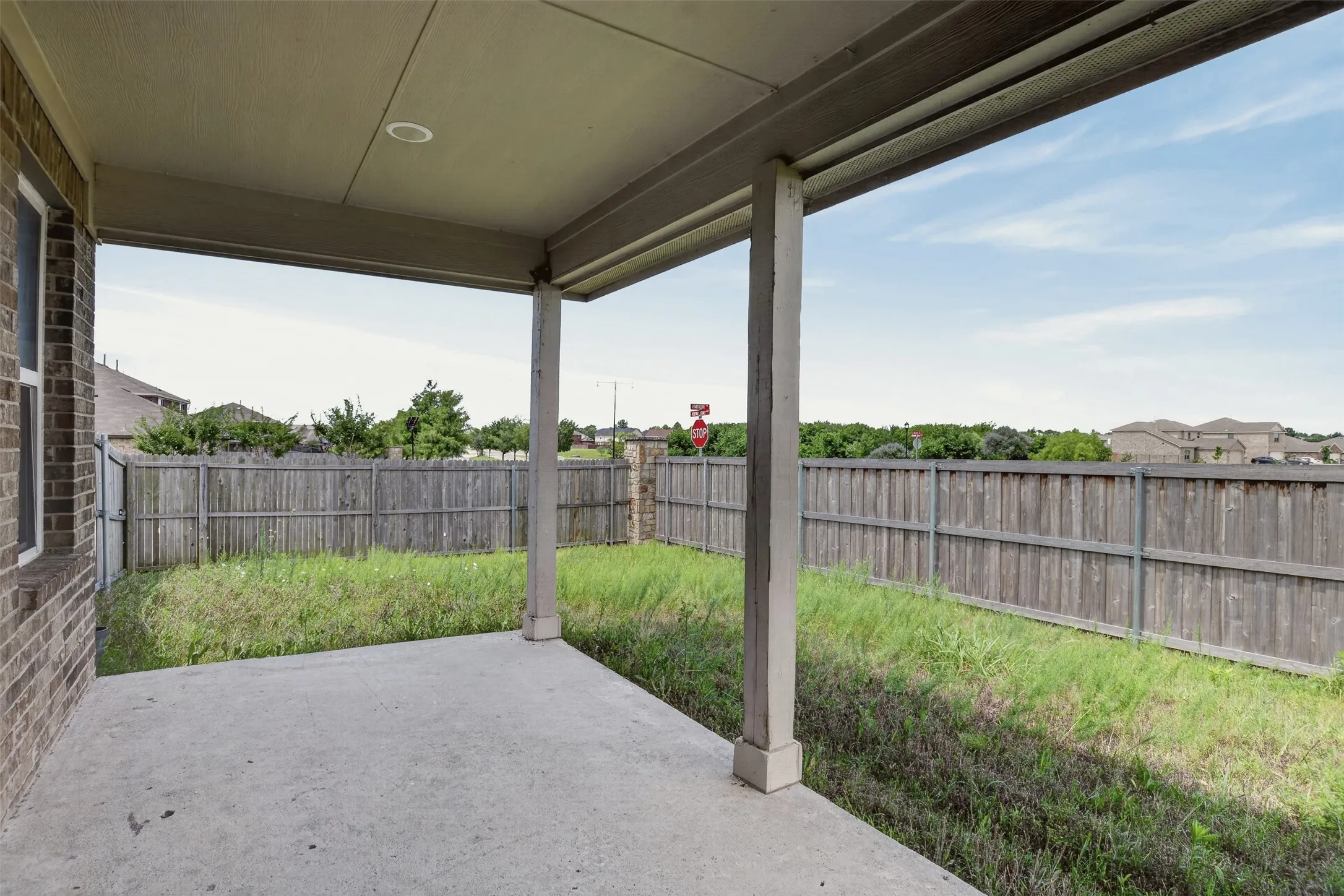 Covered concrete patio with recessed lighting, brick exterior, and a wooden privacy fence