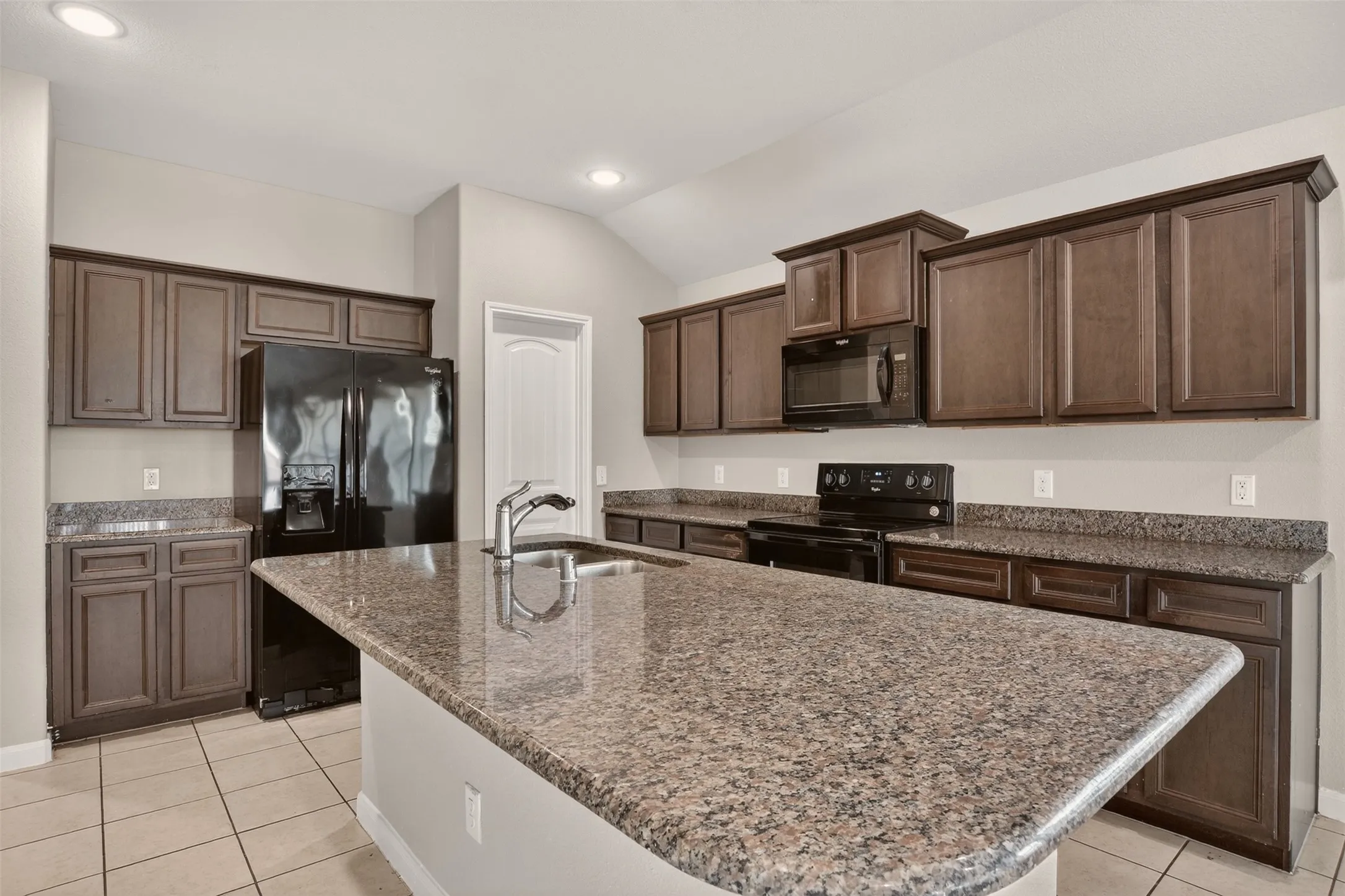 Kitchen featuring an oversized island with an undermount sink, granite countertops, and dark wood-finish cabinetry
