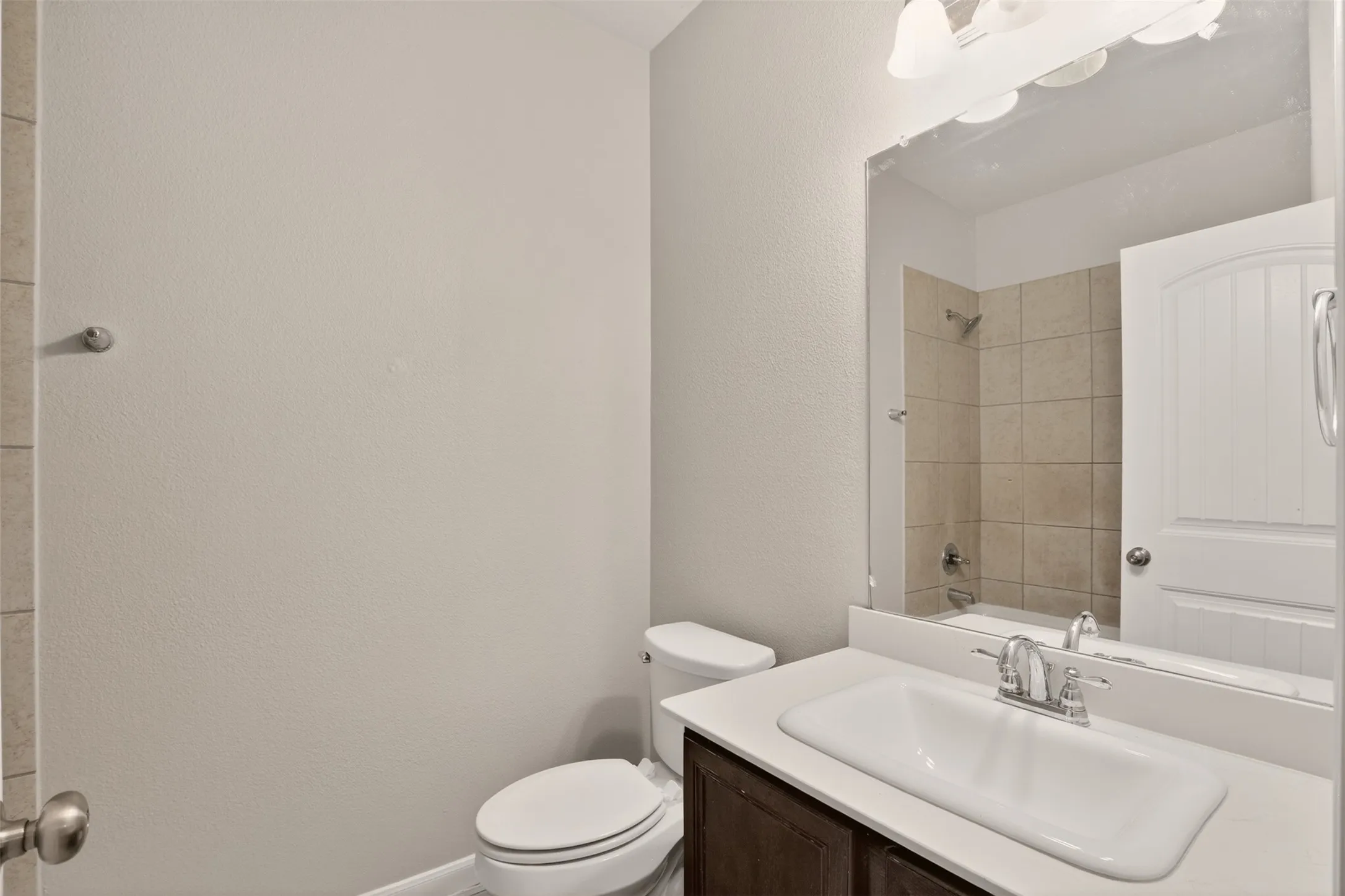 Bathroom featuring a white elongated toilet, a vanity with a dark wood-finish cabinet, a white countertop, an integrated sink, and a large wall mirror