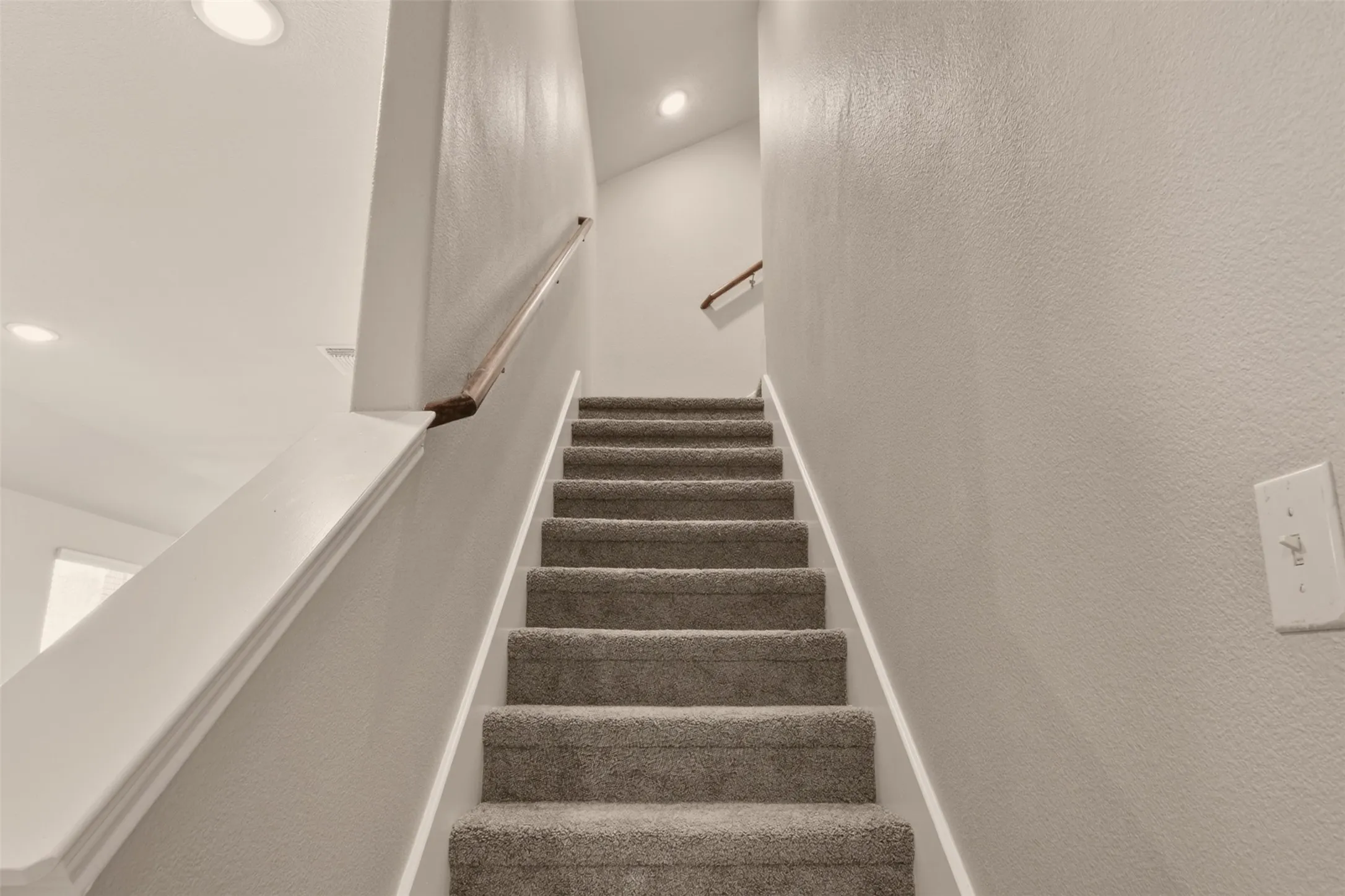 Carpeted staircase with white trim, wood handrail, and recessed lighting