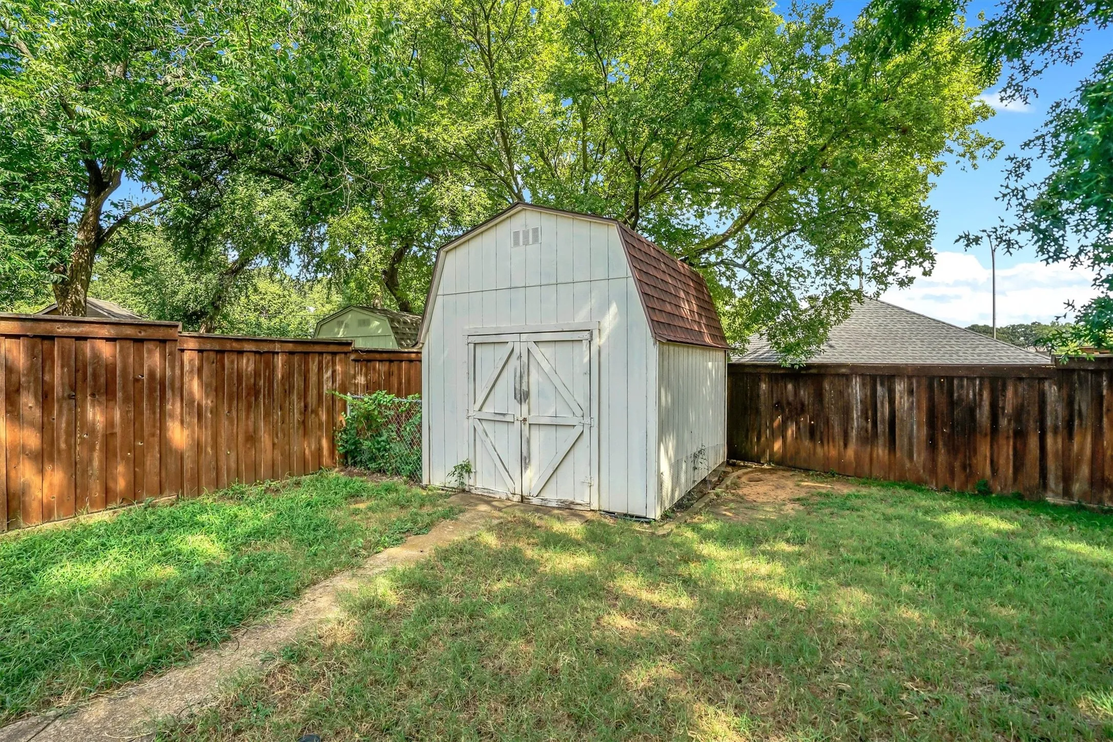Private yard featuring a storage shed with gambrel roof, double barn doors, and white siding
