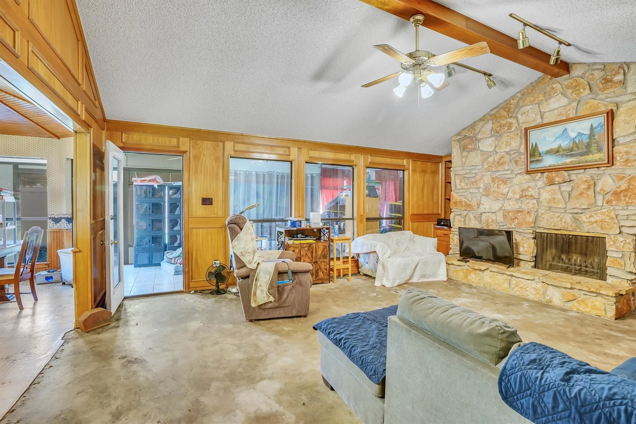 Spacious living area featuring a vaulted ceiling with exposed wood beams, a stone-clad fireplace, and extensive wood paneling