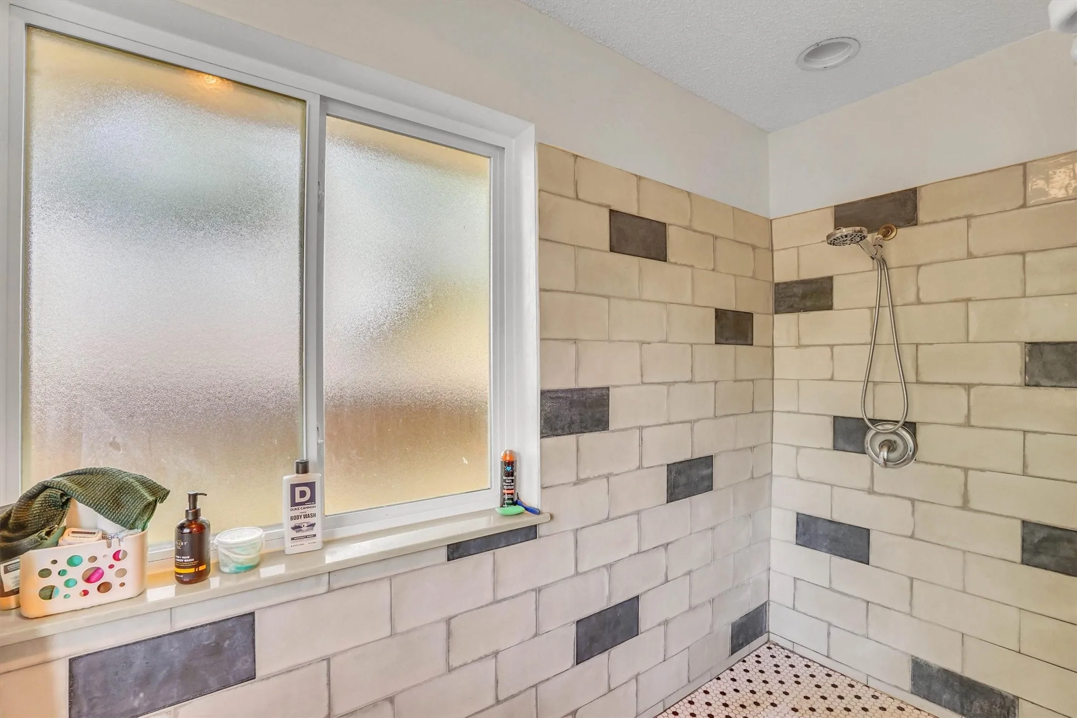Shower enclosure featuring light-toned subway tiles with contrasting dark accent tiles