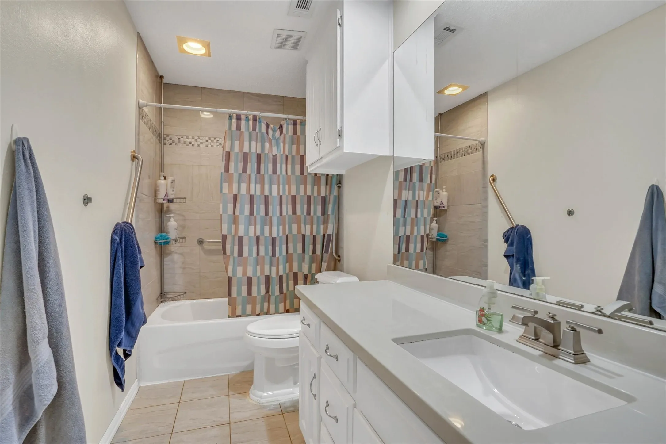 Bathroom featuring a white vanity with an integrated sink, a large mirror, and overhead cabinetry