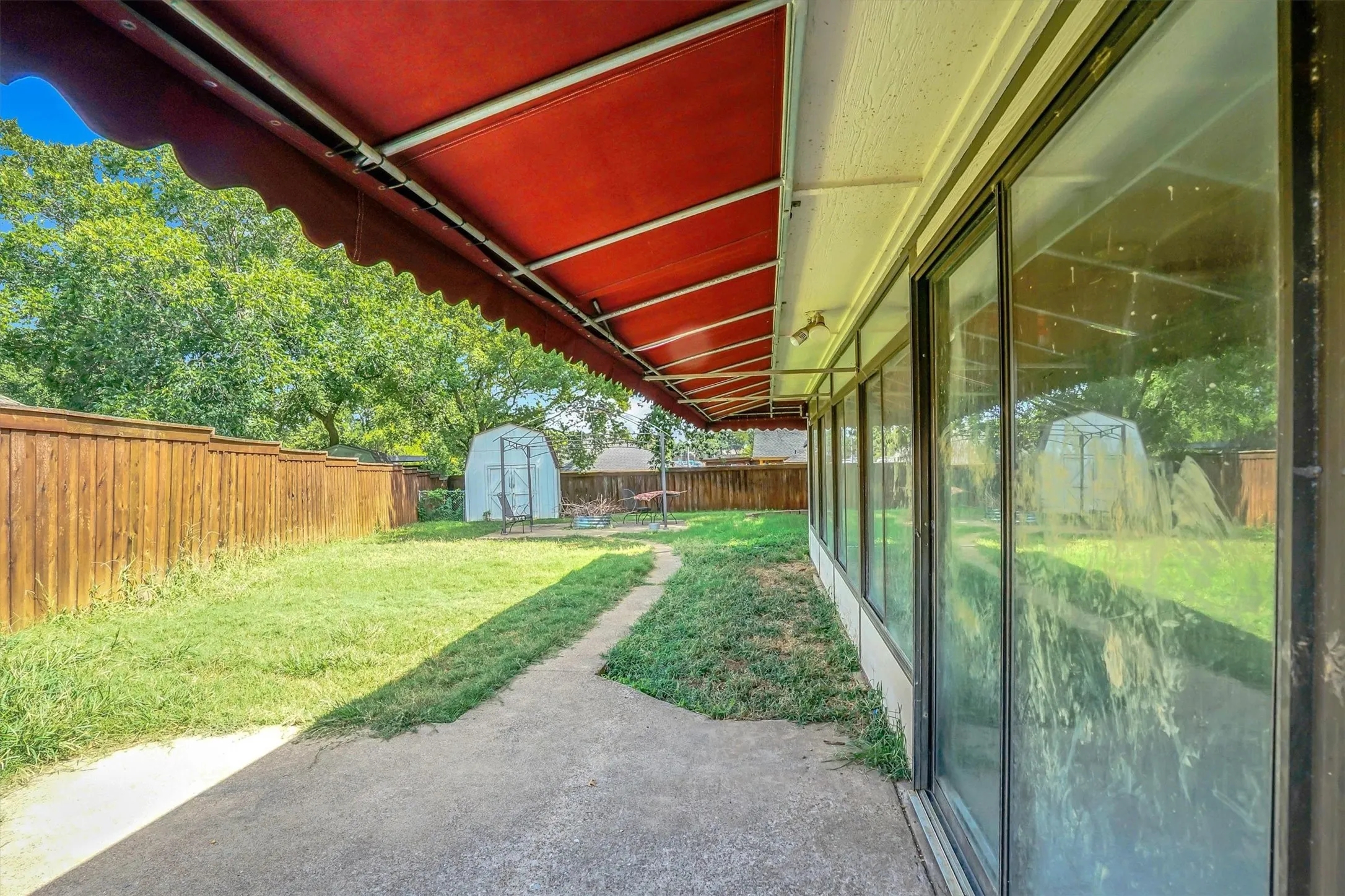 Patio space featuring a red retractable awning, concrete flooring, and a series of large glass windows
