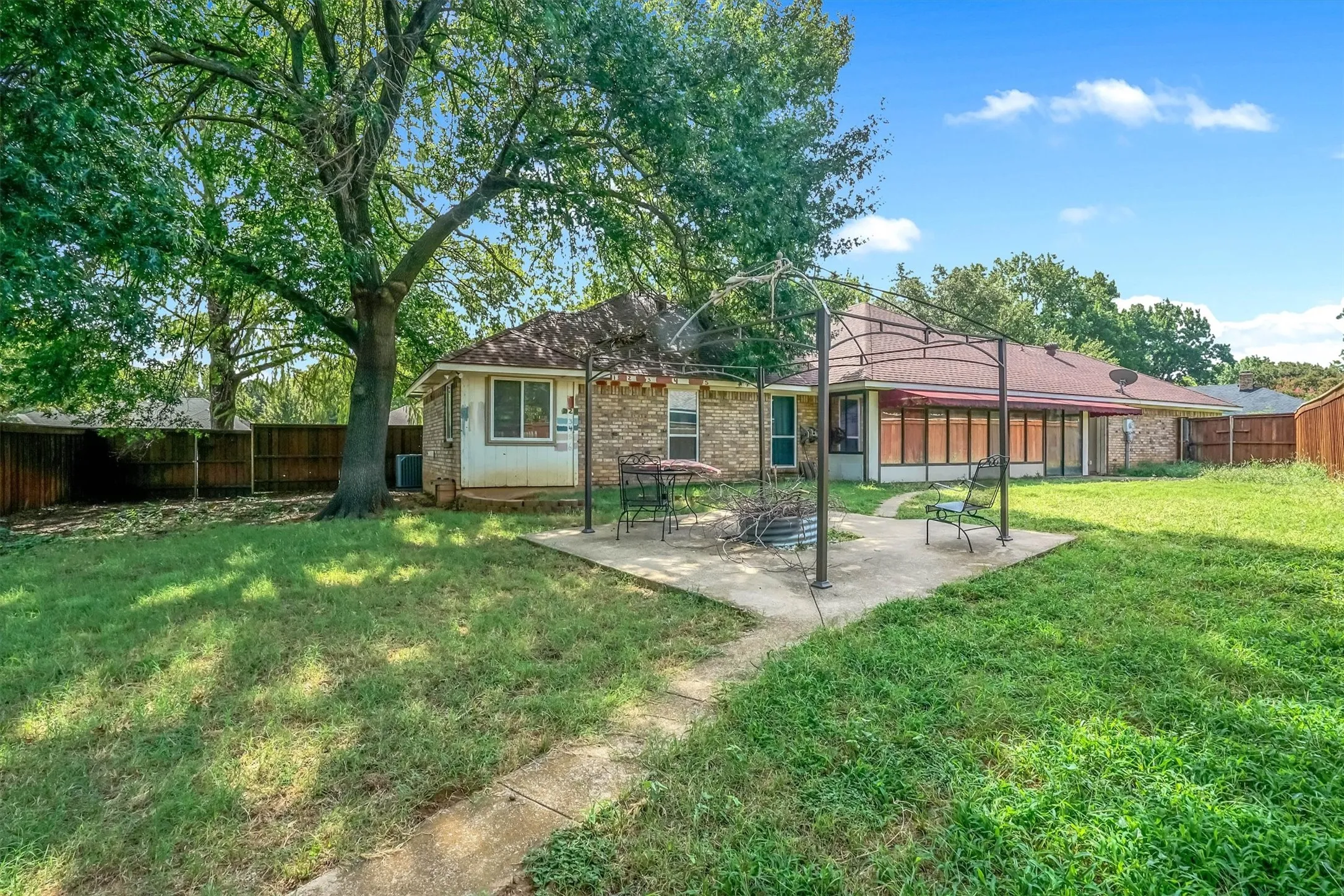 Expansive backyard featuring a concrete patio, mature trees, and a metal pergola structure