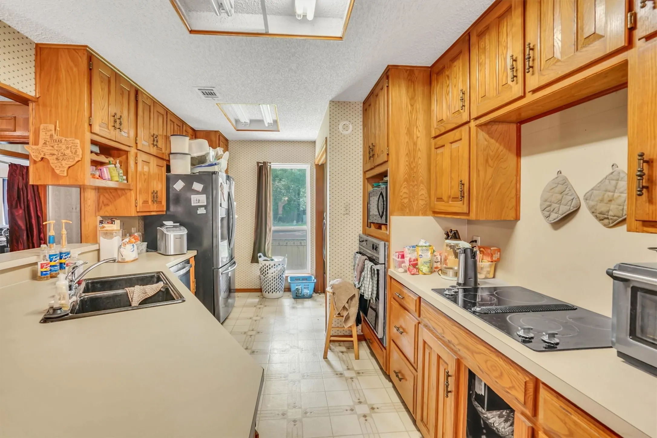 Kitchen featuring extensive light wood cabinetry, light countertops, dual skylights, a built-in microwave, and a black cooktop