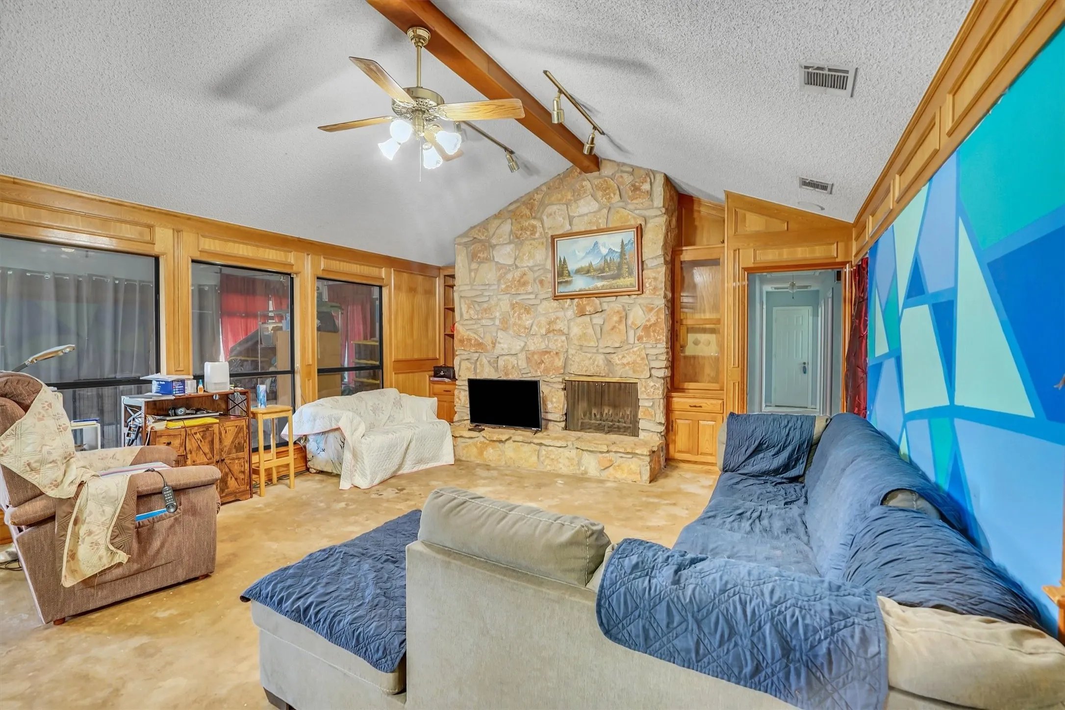 Living area featuring a floor-to-ceiling stone fireplace, vaulted ceiling with exposed wood beam, wood-trimmed windows, and built-in cabinetry