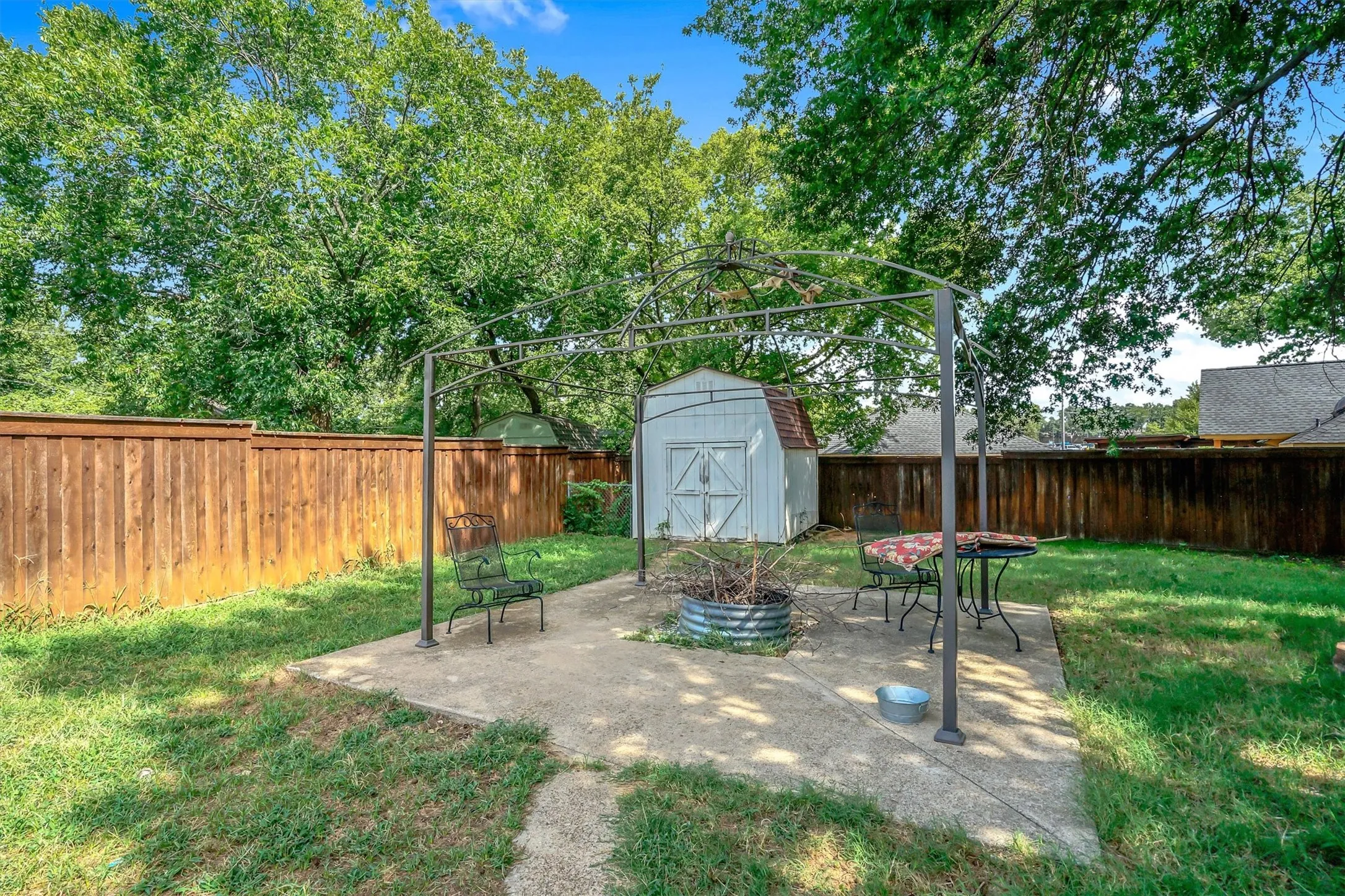 Expansive backyard featuring a concrete patio, mature trees, a wooden privacy fence, and a utility shed