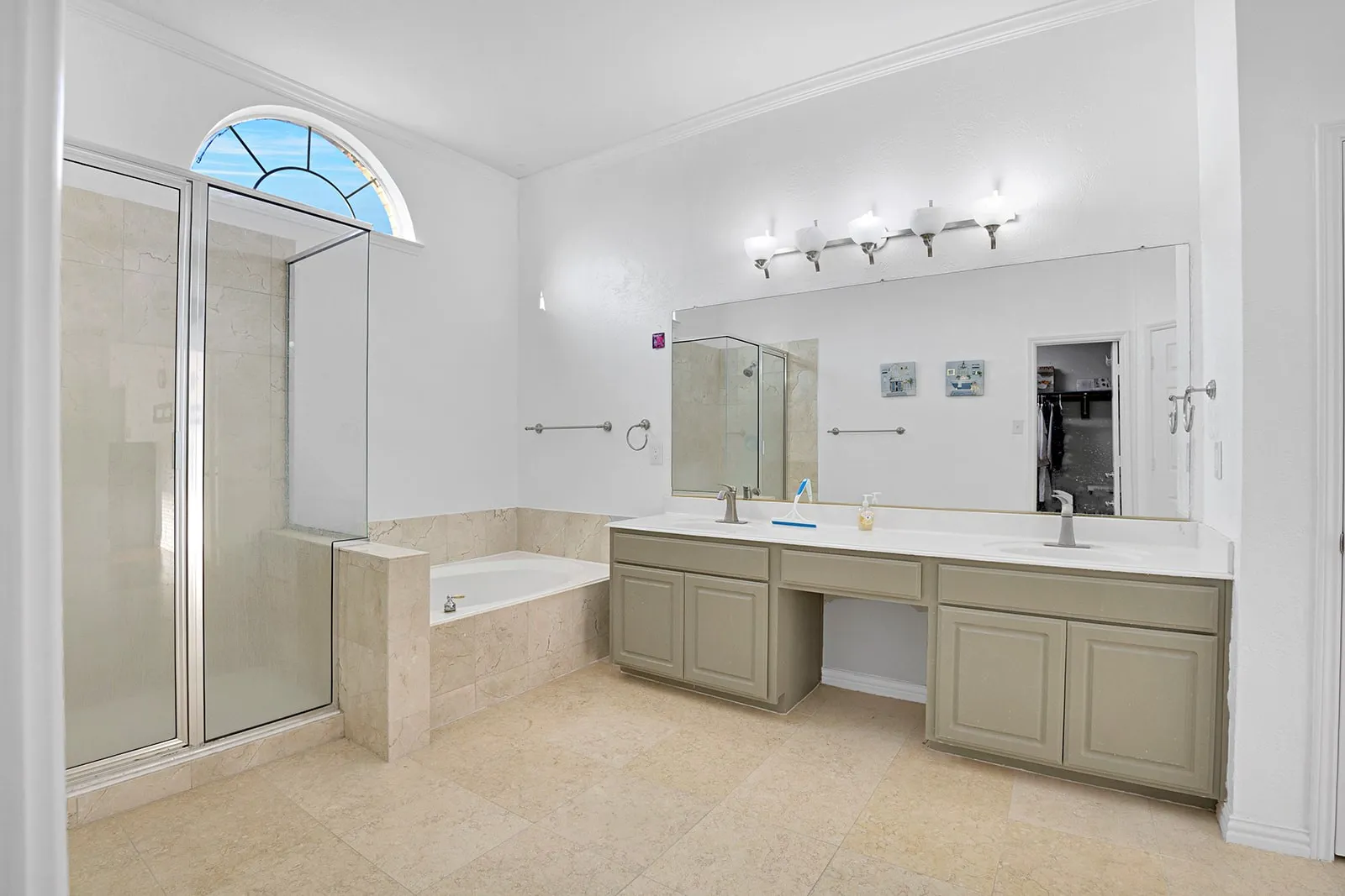 Bathroom featuring dual vanities with integrated sinks, a built-in tub, a glass-enclosed shower, arched transom windows, and tile flooring