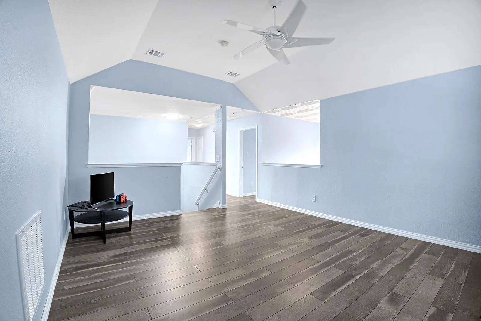 Vaulted ceiling room featuring a large arched window with horizontal blinds, wood-finish flooring, a ceiling fan with integrated lighting, and light blue wall tones