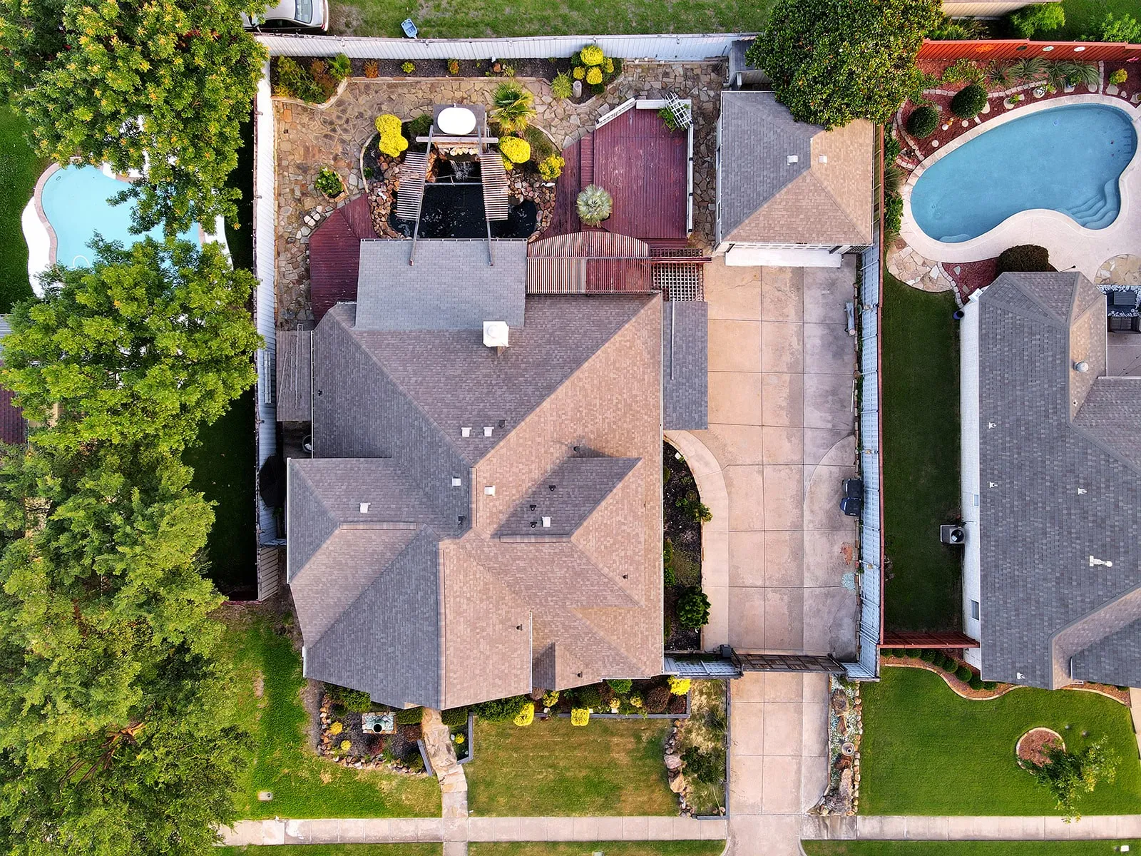 Expansive property featuring a multi-gabled roofline, concrete driveway, and a private backyard with a decorative pond and wooden decking