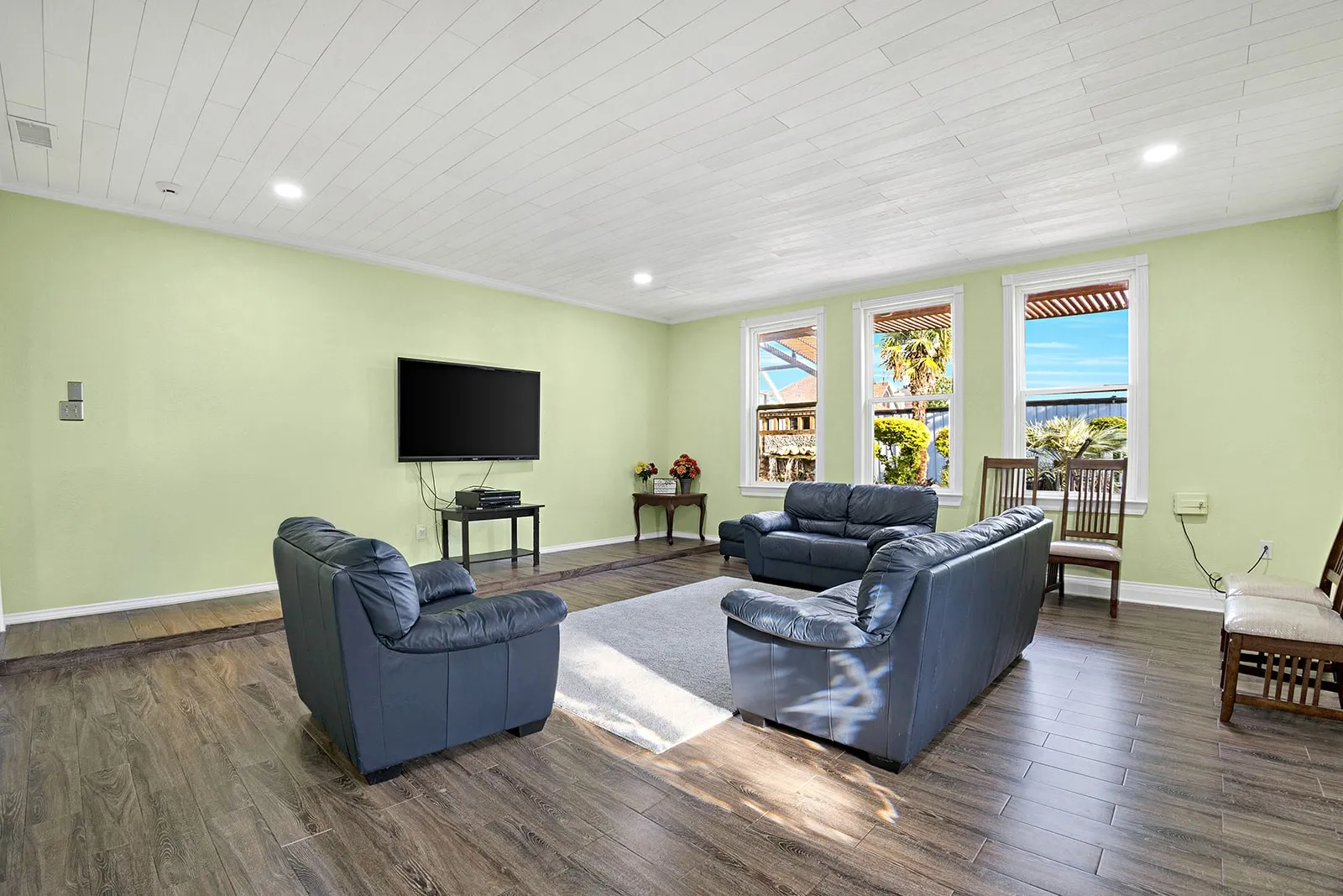 Spacious interior featuring wood-finish flooring, a kitchen island with seating, white cabinetry, a tiled backsplash, and an open staircase with white balusters