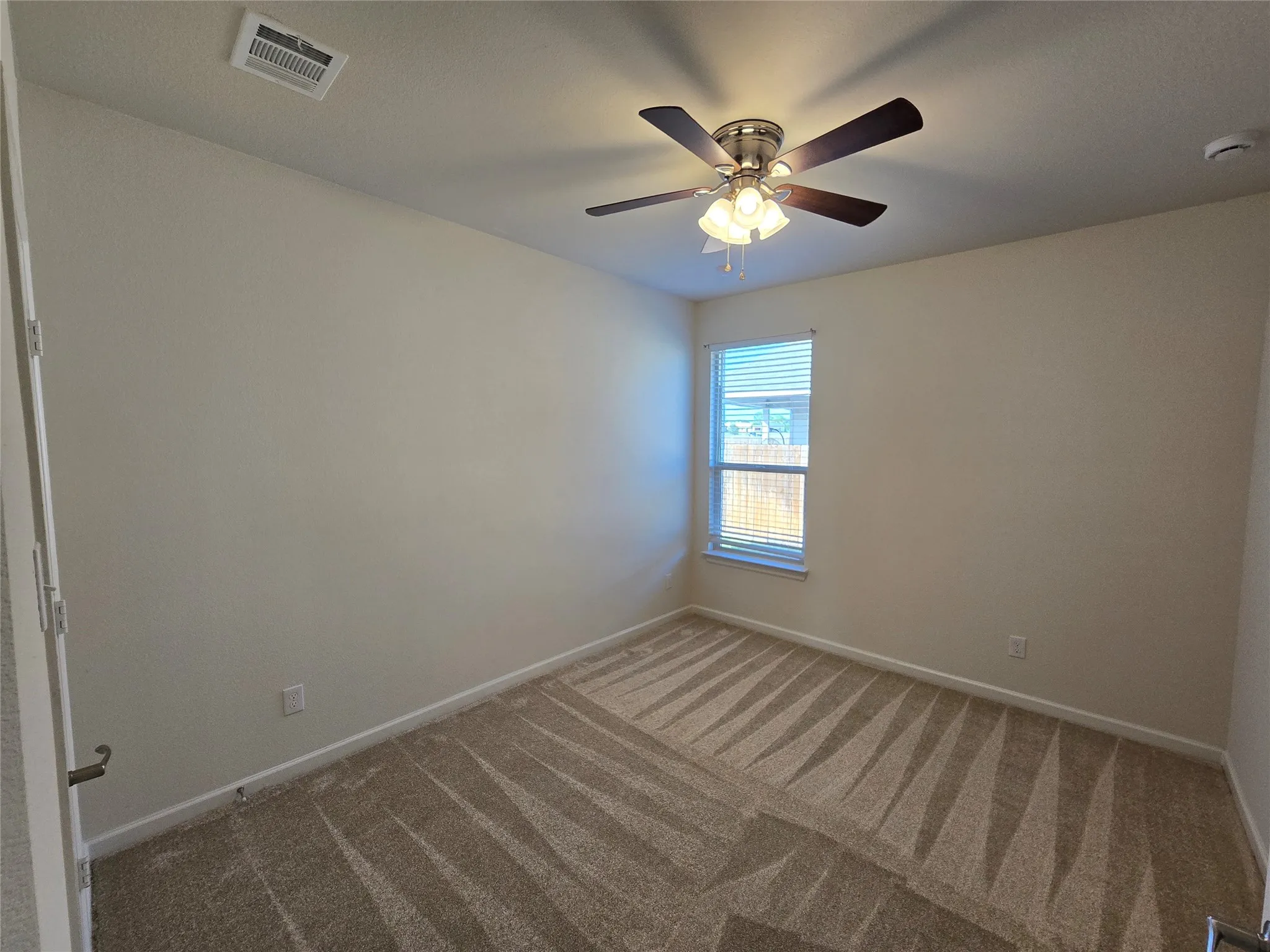 Neutral-toned room featuring patterned carpeting, a window with blinds, and a ceiling fan with integrated lighting
