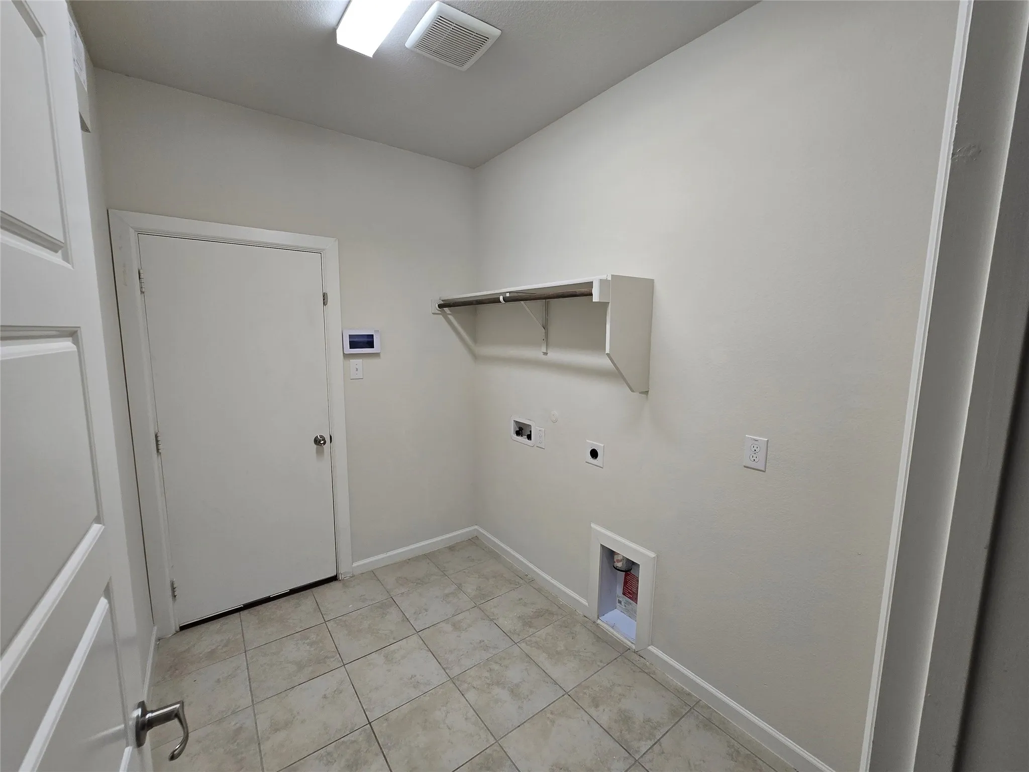 Utility room featuring light-toned tile flooring, neutral wall tones, a built-in shelf with hanging rod, and essential appliance hookups