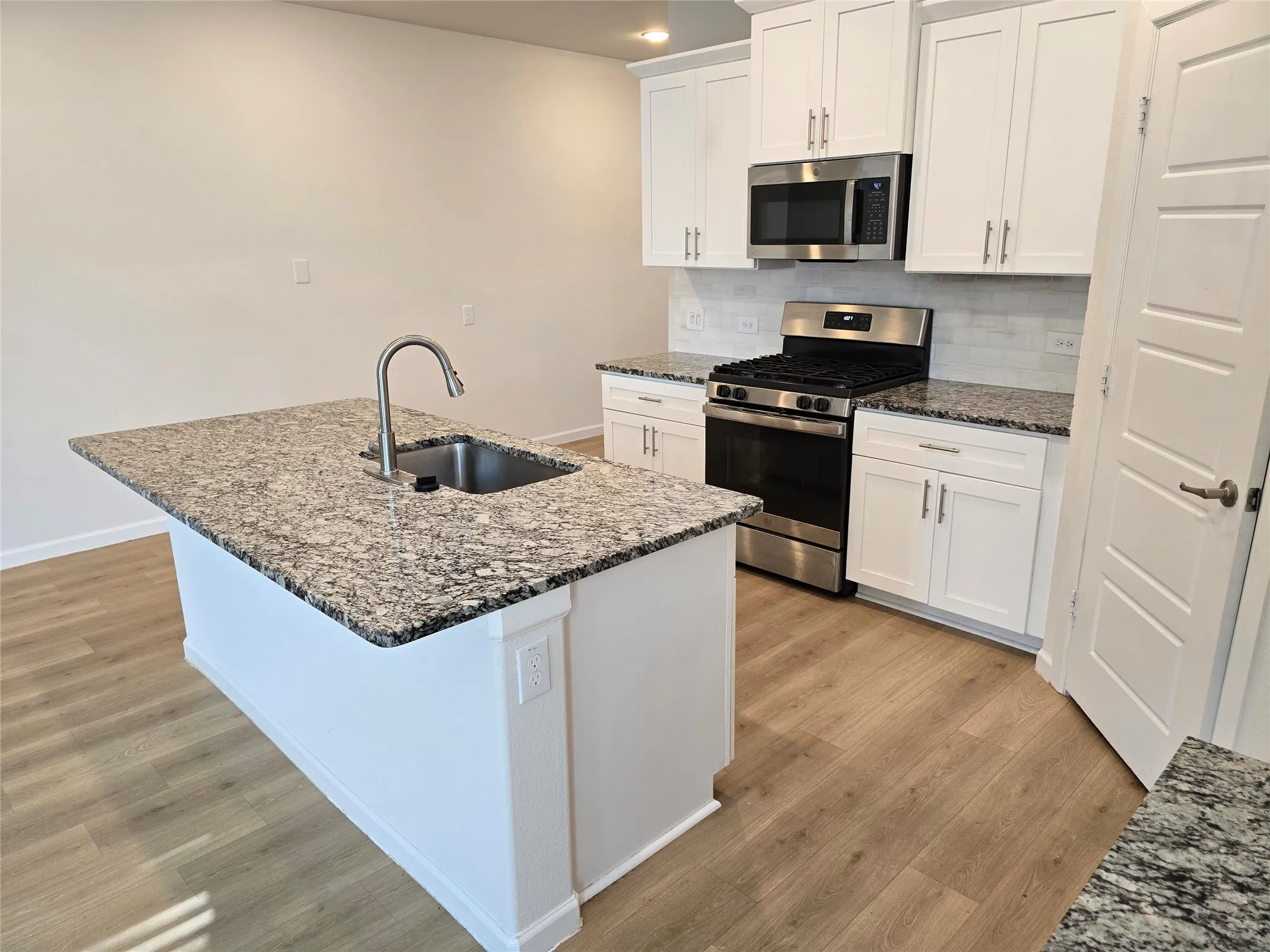 Kitchen featuring an island with a stainless steel sink, granite countertops, white cabinetry, a stainless steel gas range, and wood-finish flooring