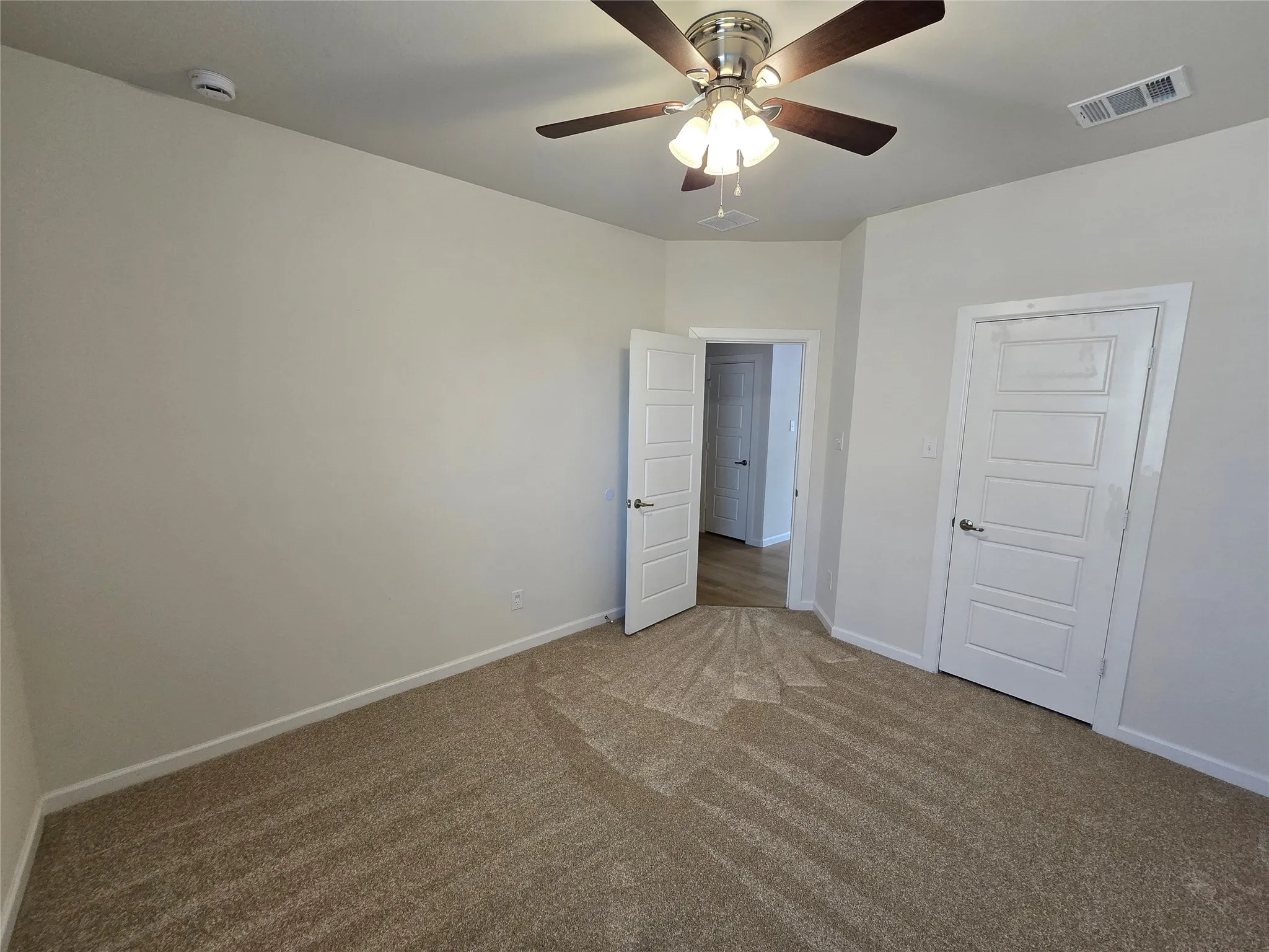 Carpeted interior room featuring a ceiling fan with light fixture, white paneled doors with chrome hardware, white baseboards, and neutral wall paint