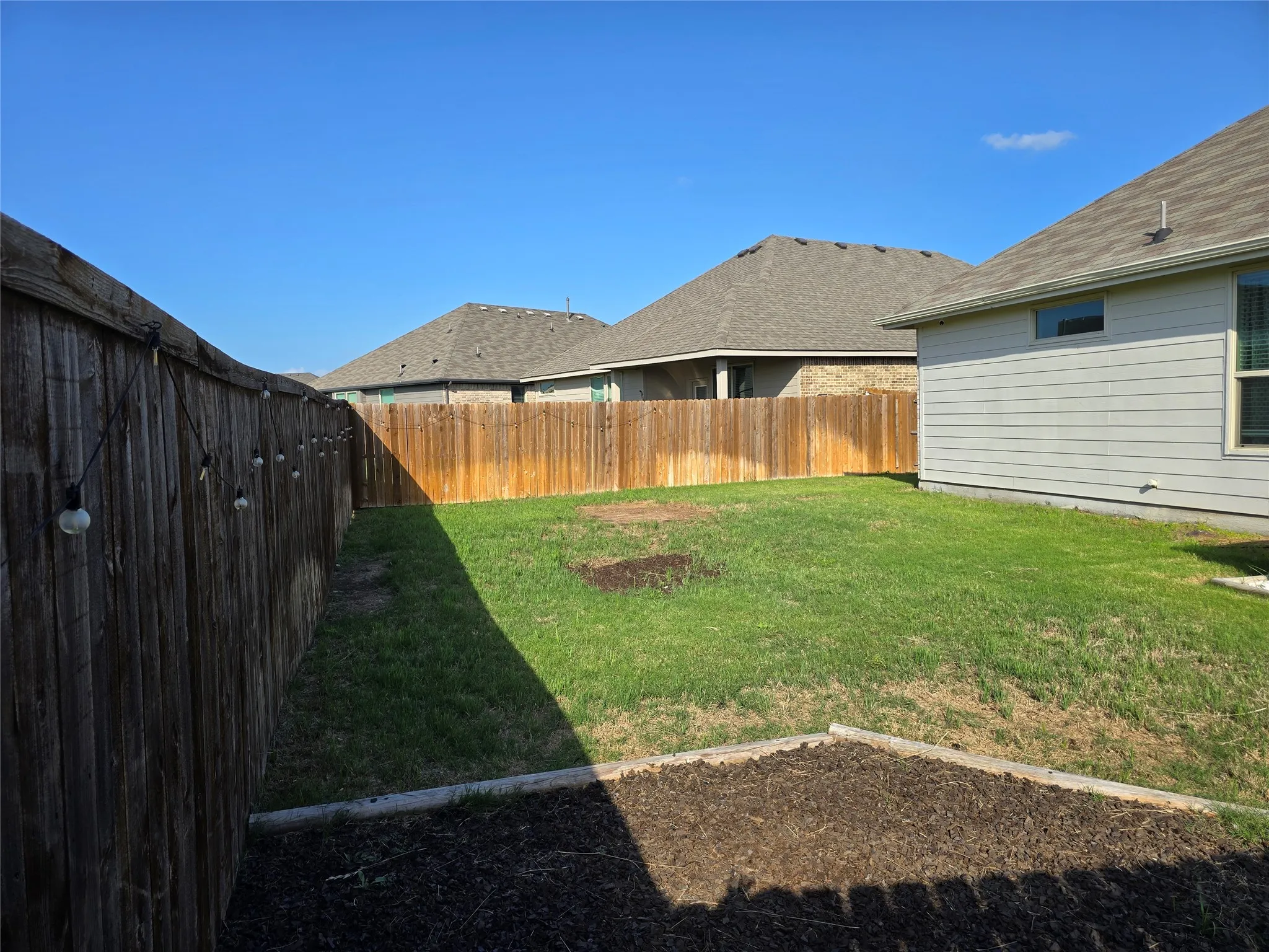Private backyard featuring a wooden privacy fence, a manicured lawn, and a raised garden bed