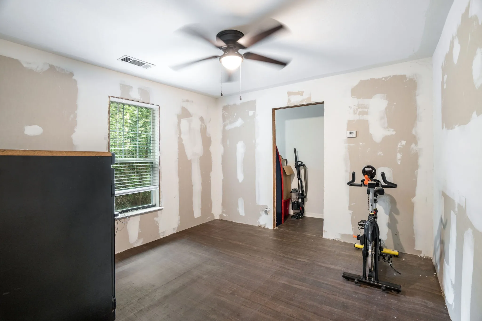 Room featuring dark wood-finish flooring, a ceiling fan with integrated lighting, and a window with horizontal blinds