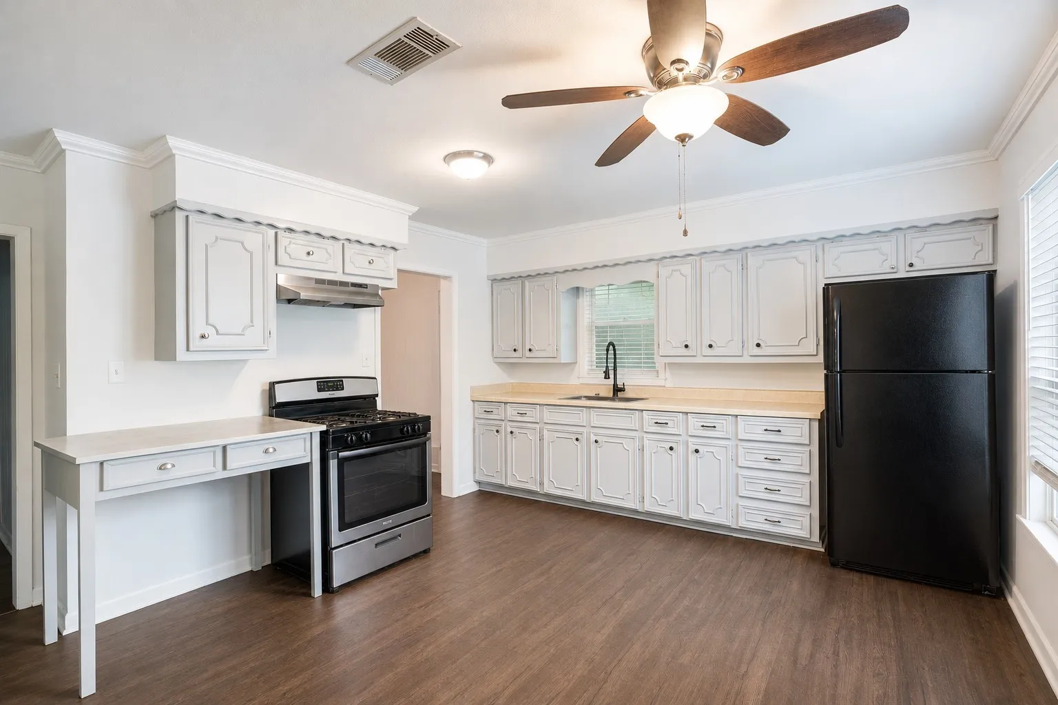 Kitchen featuring wood-finish flooring, light-toned cabinetry, a ceiling fan, a gas range with a stainless steel hood, and a built-in desk