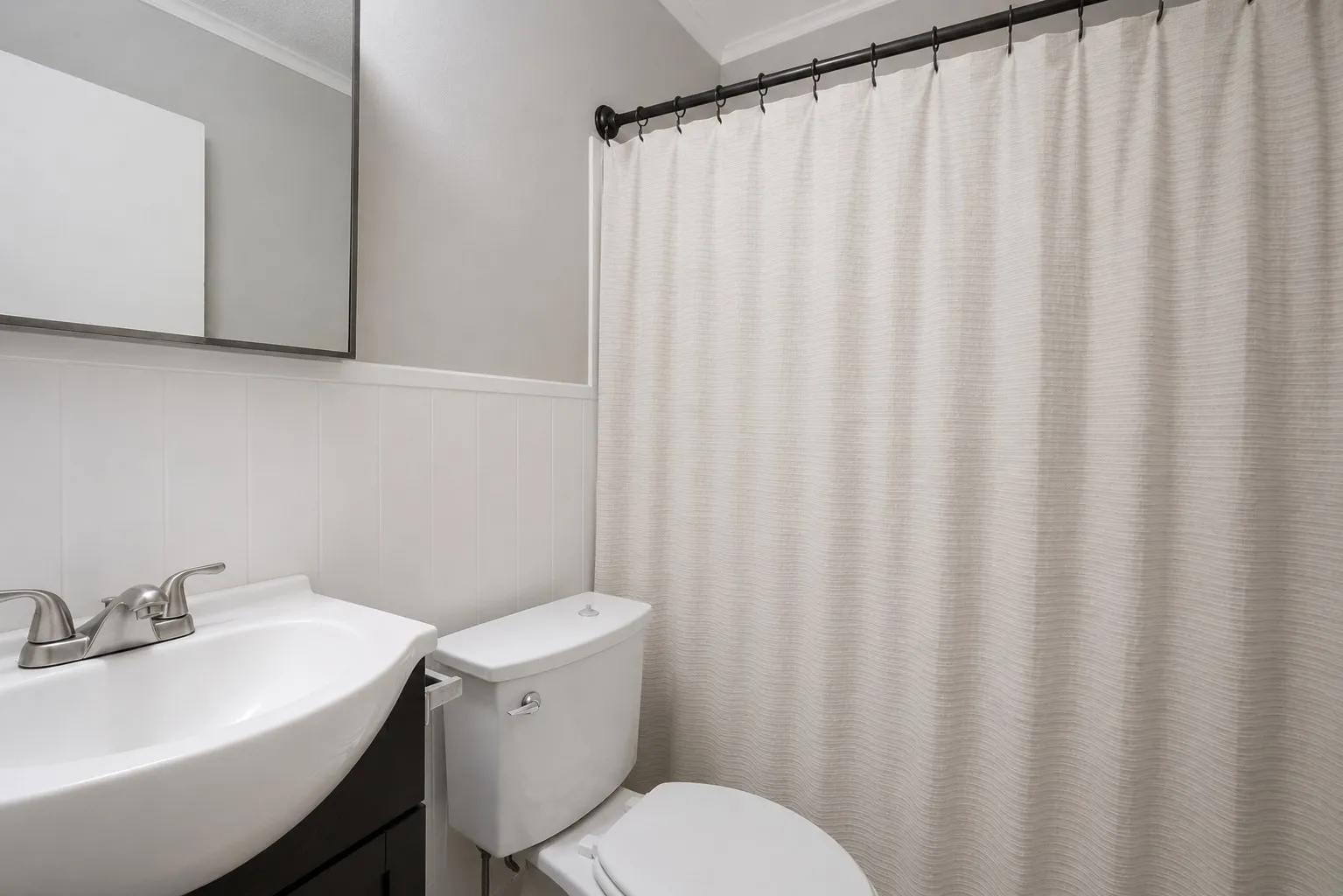Bathroom featuring wainscoting, a wall-mounted mirror, a modern vanity with an integrated sink, a two-piece toilet, and a dark-finish shower rod