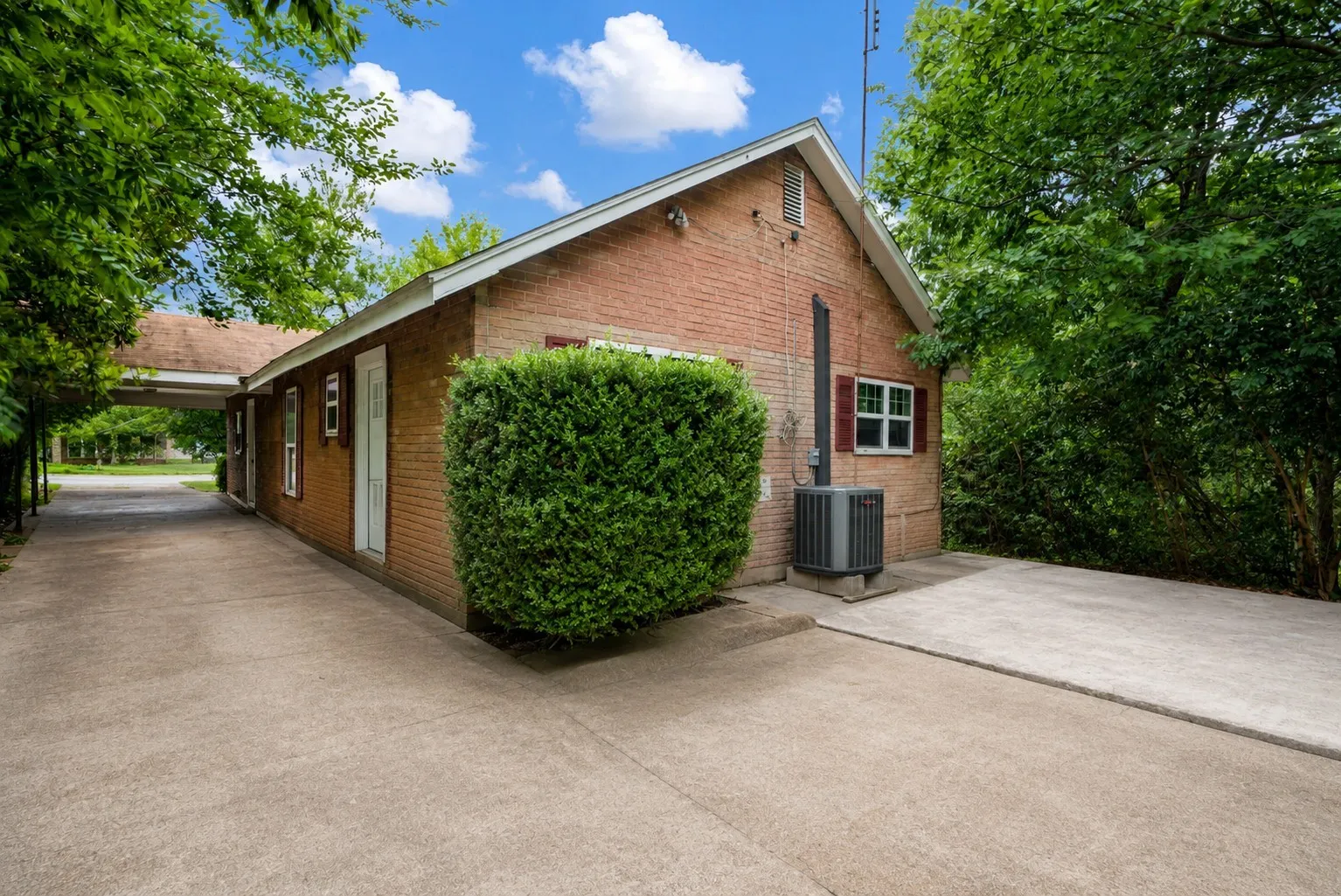 Brick exterior featuring a covered carport, concrete driveway, and mature landscaping