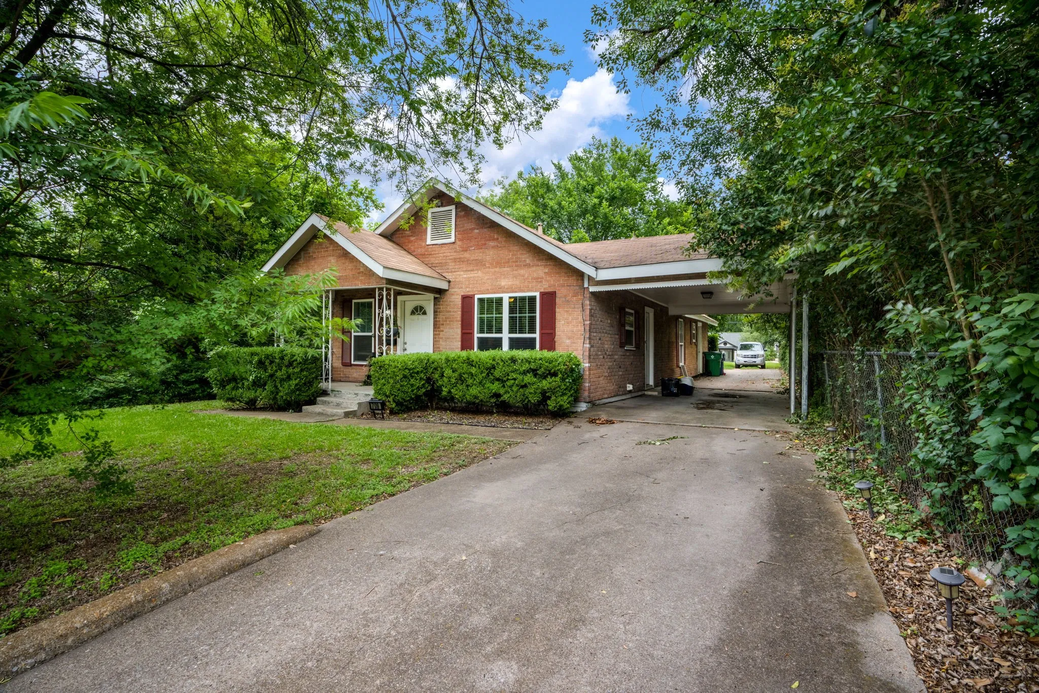 Brick exterior with white front door, covered front porch, red window shutters, and an attached carport