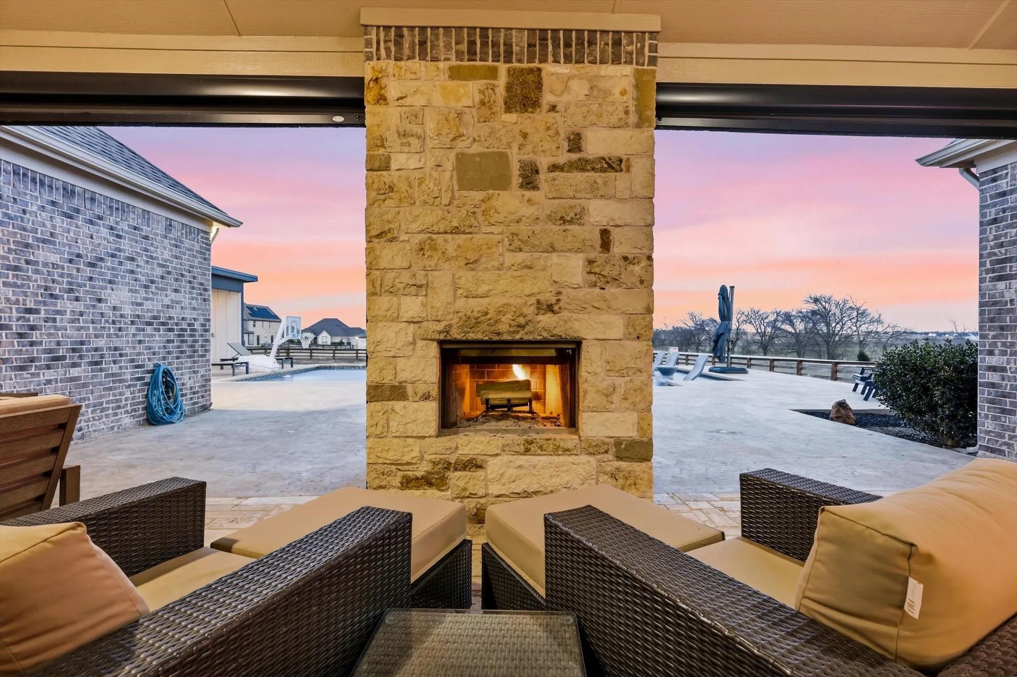 Outdoor living space featuring a stone fireplace, integrated ceiling lighting, and a paved patio extending to a swimming pool