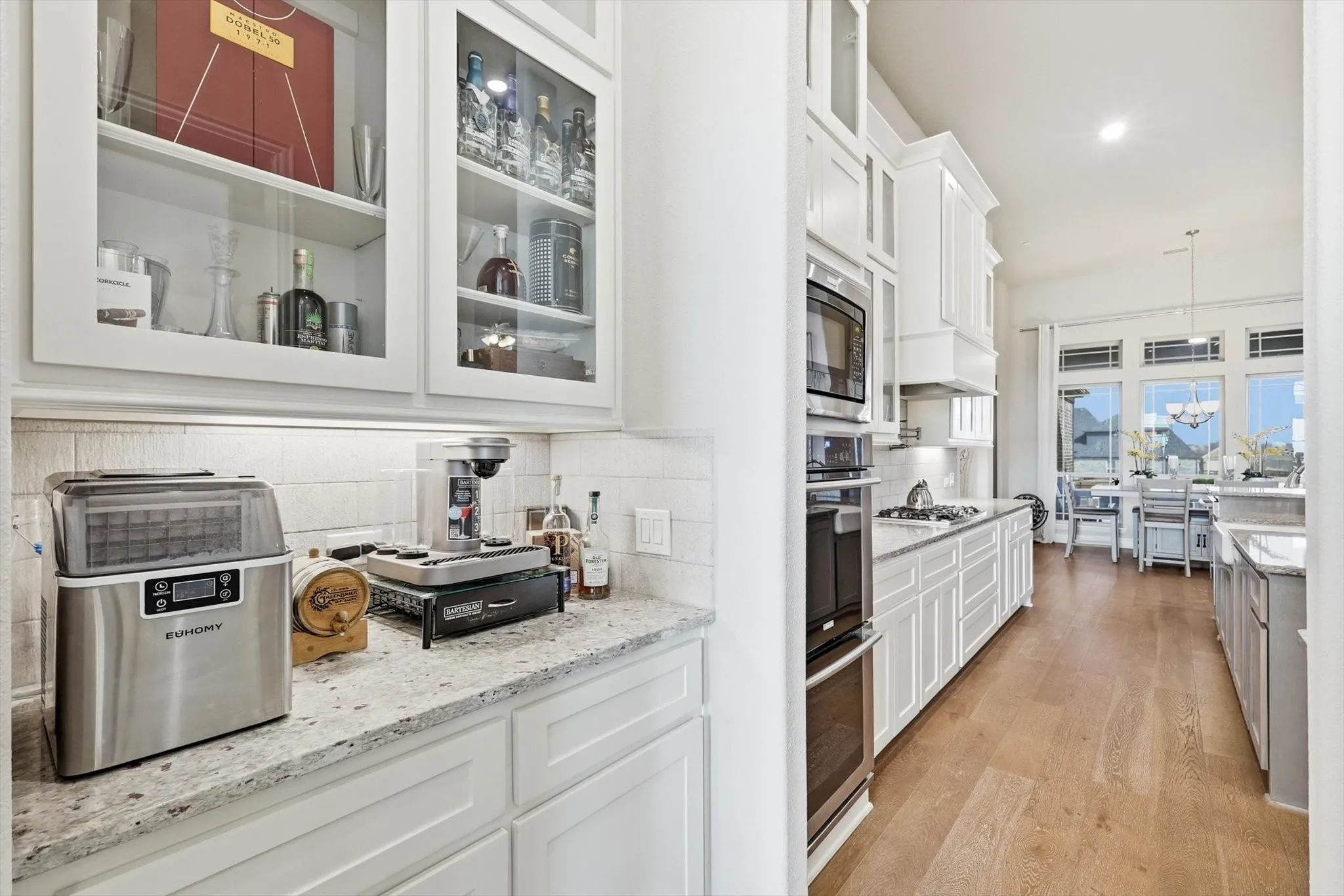Modern kitchen featuring white cabinetry, light-toned countertops, wood-finish flooring, built-in stainless steel appliances, and a tile backsplash