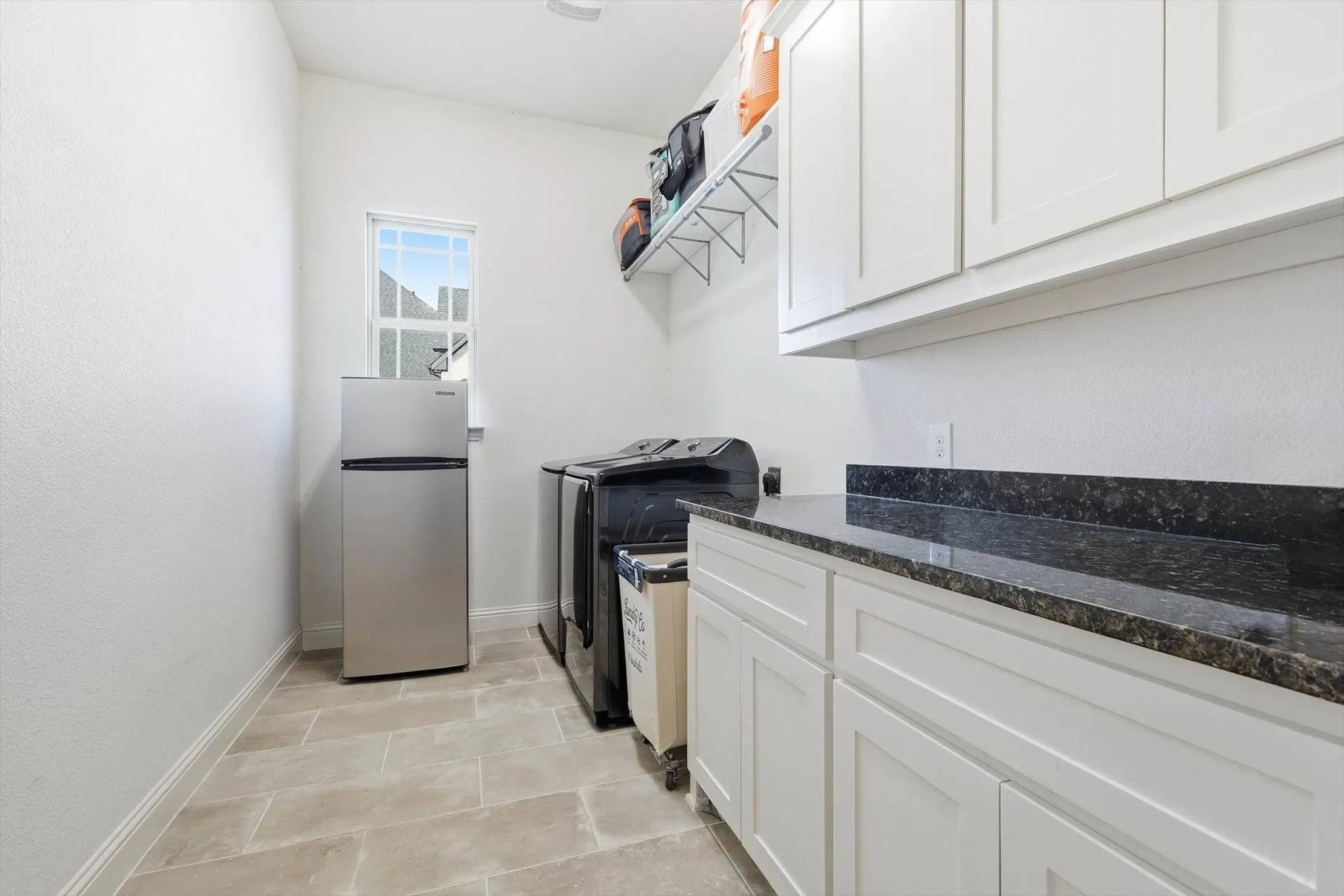 Laundry room featuring tile flooring, white cabinetry, dark stone countertops, and a window providing natural light
