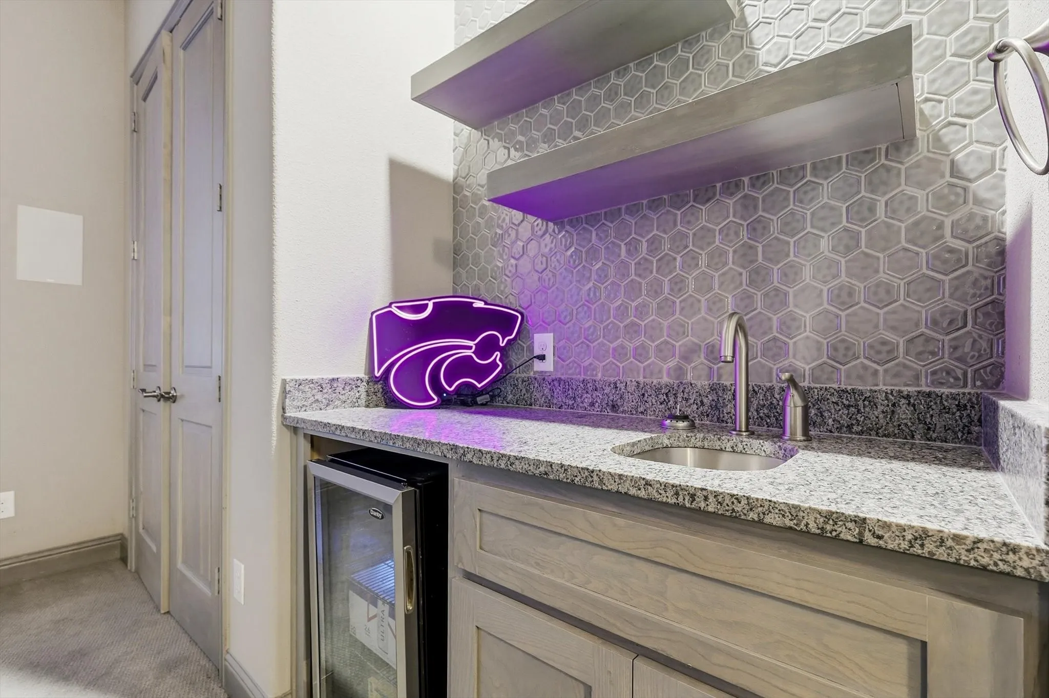 Wet bar with granite countertops, hexagonal tile backsplash, stainless steel sink with gooseneck faucet, custom cabinetry, and built-in beverage refrigerator