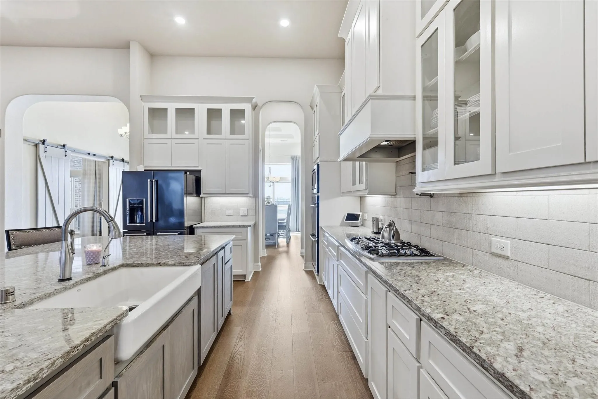 Gourmet kitchen featuring a white apron-front sink, granite countertops, white subway tile backsplash, and wood-finish flooring