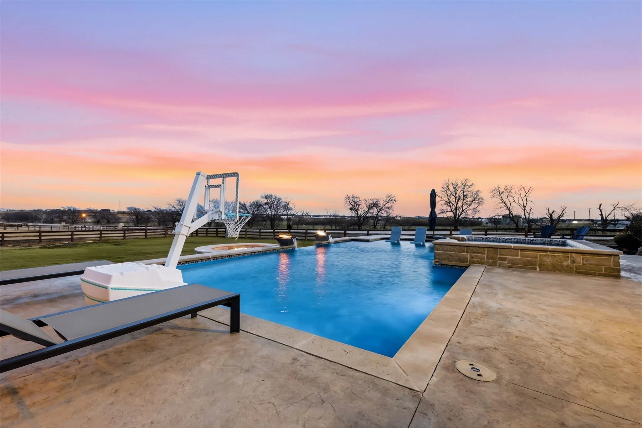 Expansive outdoor living area featuring a sparkling swimming pool, integrated spa, and a stone-clad fire pit