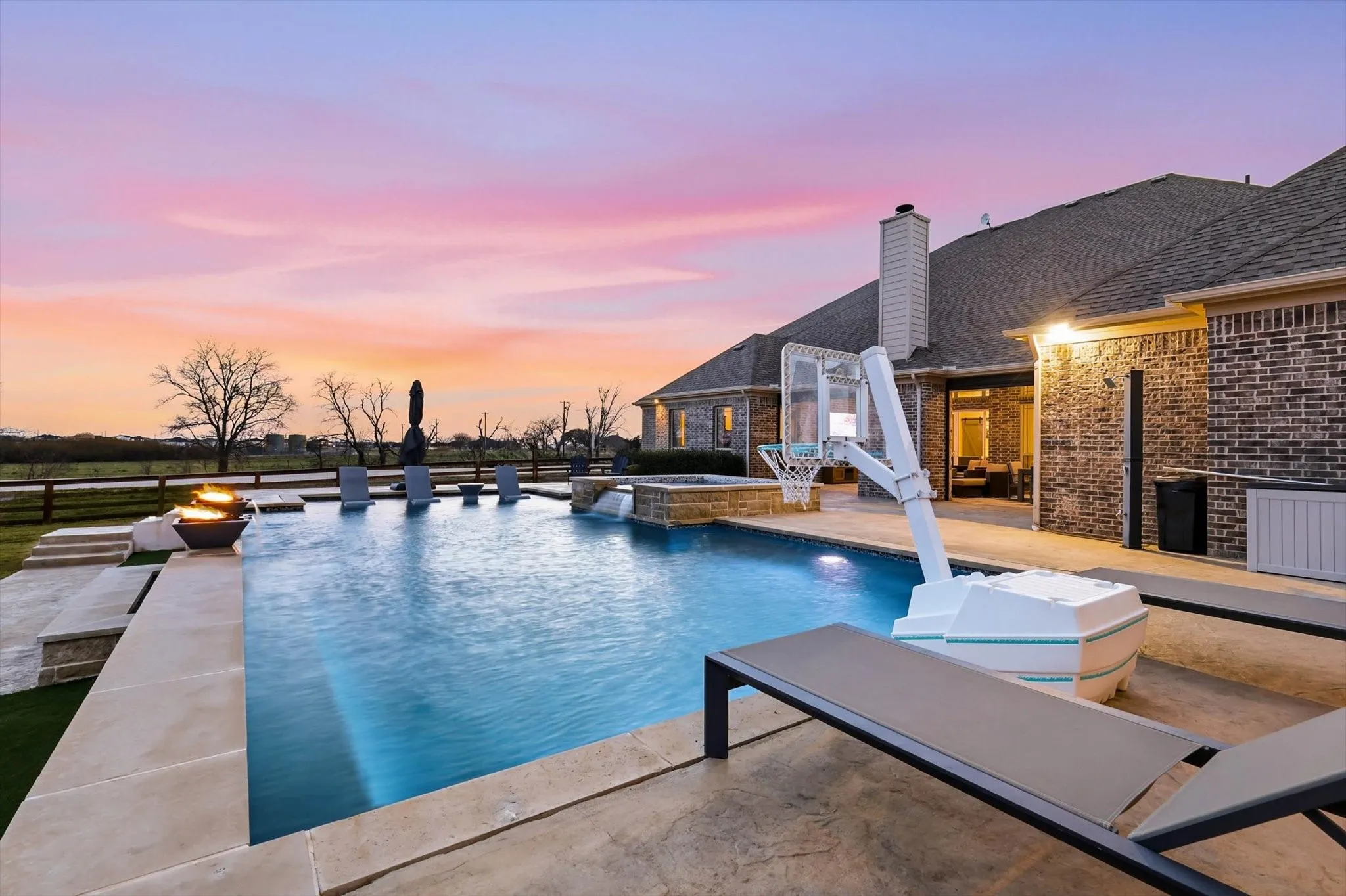 Outdoor living space featuring a swimming pool with integrated spa, a fire pit, extensive concrete and stone paving, and a brick-sided residence