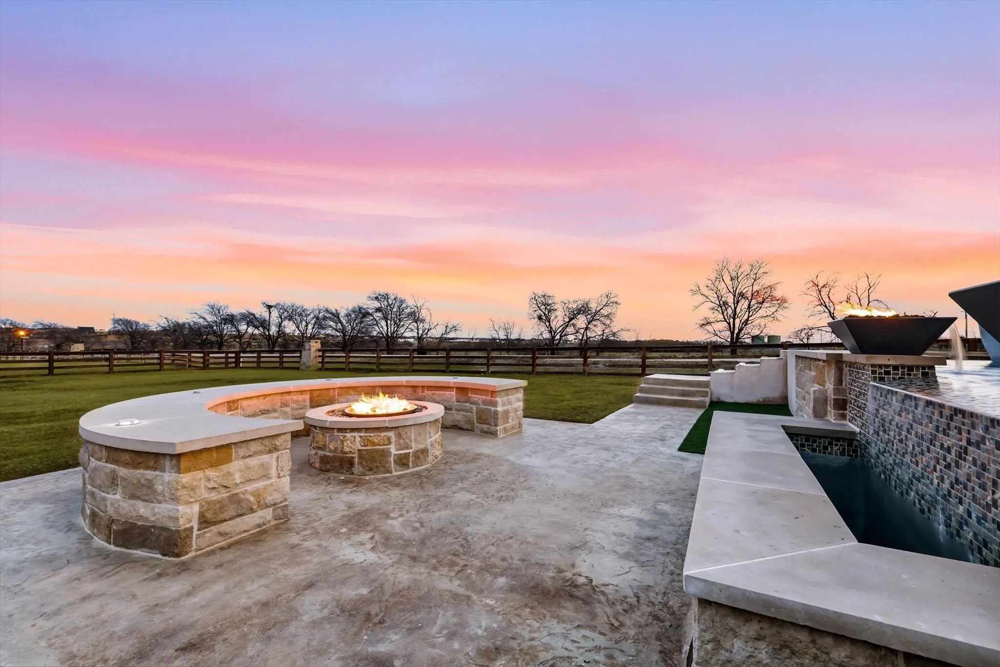 Expansive concrete patio featuring a built-in stone fire pit with integrated seating