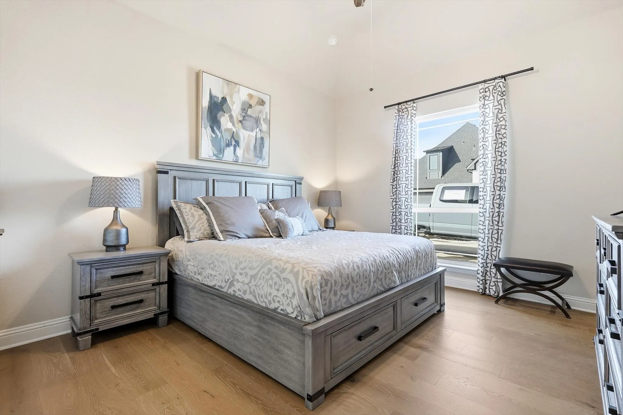 Spacious room featuring vaulted ceilings, light wood-finish flooring, and a large window with curtain rod and patterned drapes