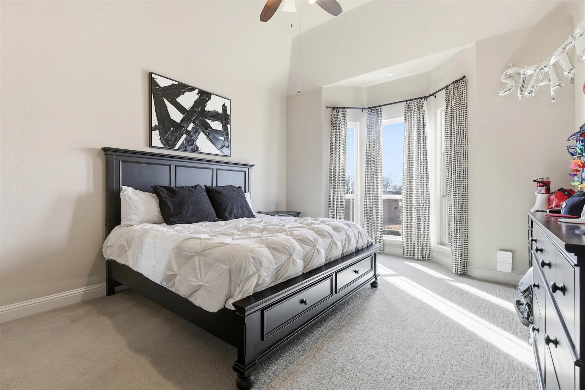 Spacious room featuring vaulted ceilings, a bay window with drapes, and neutral wall tones